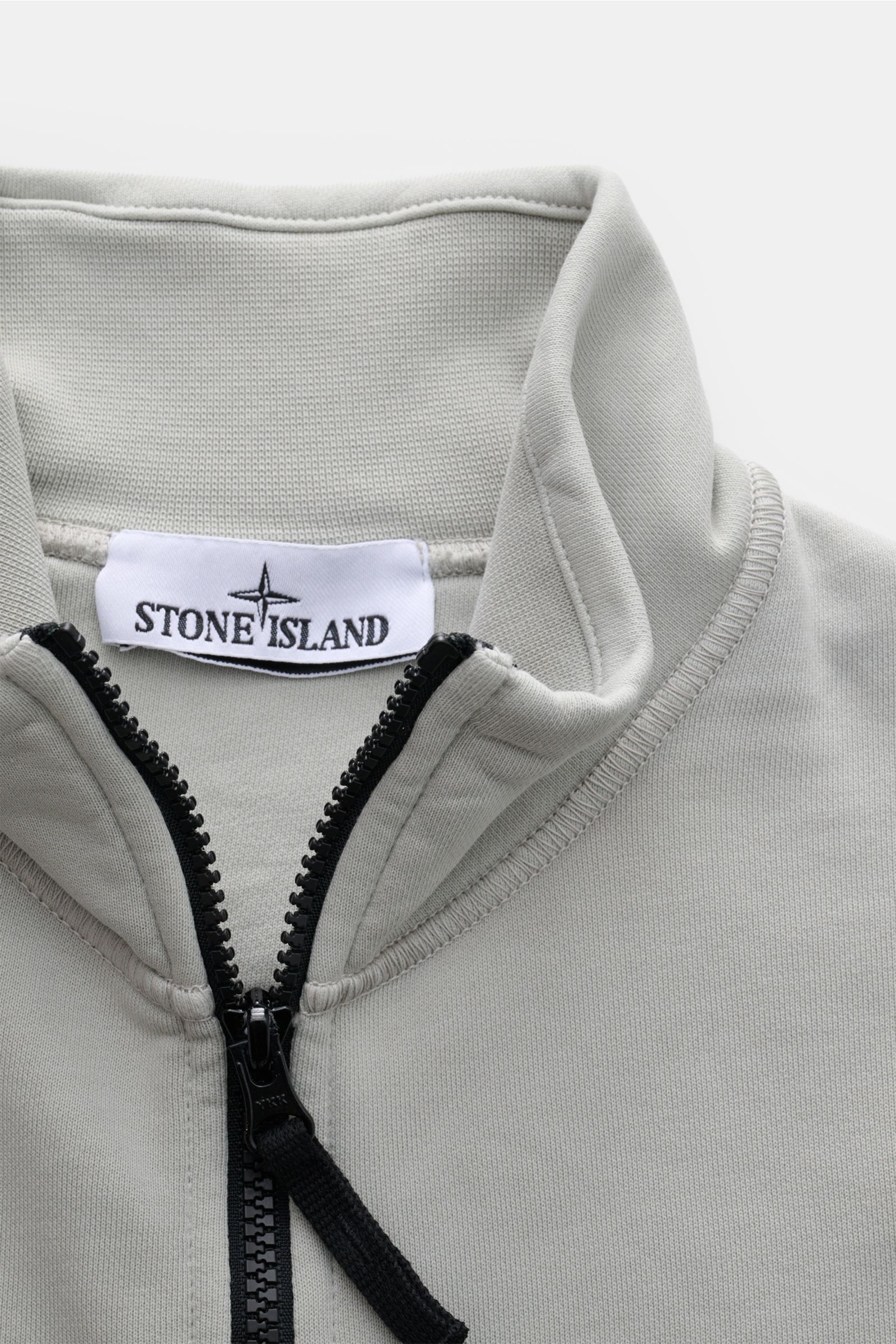 Stone Island Sweatjacke hellgrau, Detailaufnahme von oben, hochschließender Stehkragen, robuster Reißverschluss, weiche Baumwolle, garment dyed, Regular Fit, mit Kompass-Badge und Rippbündchen.