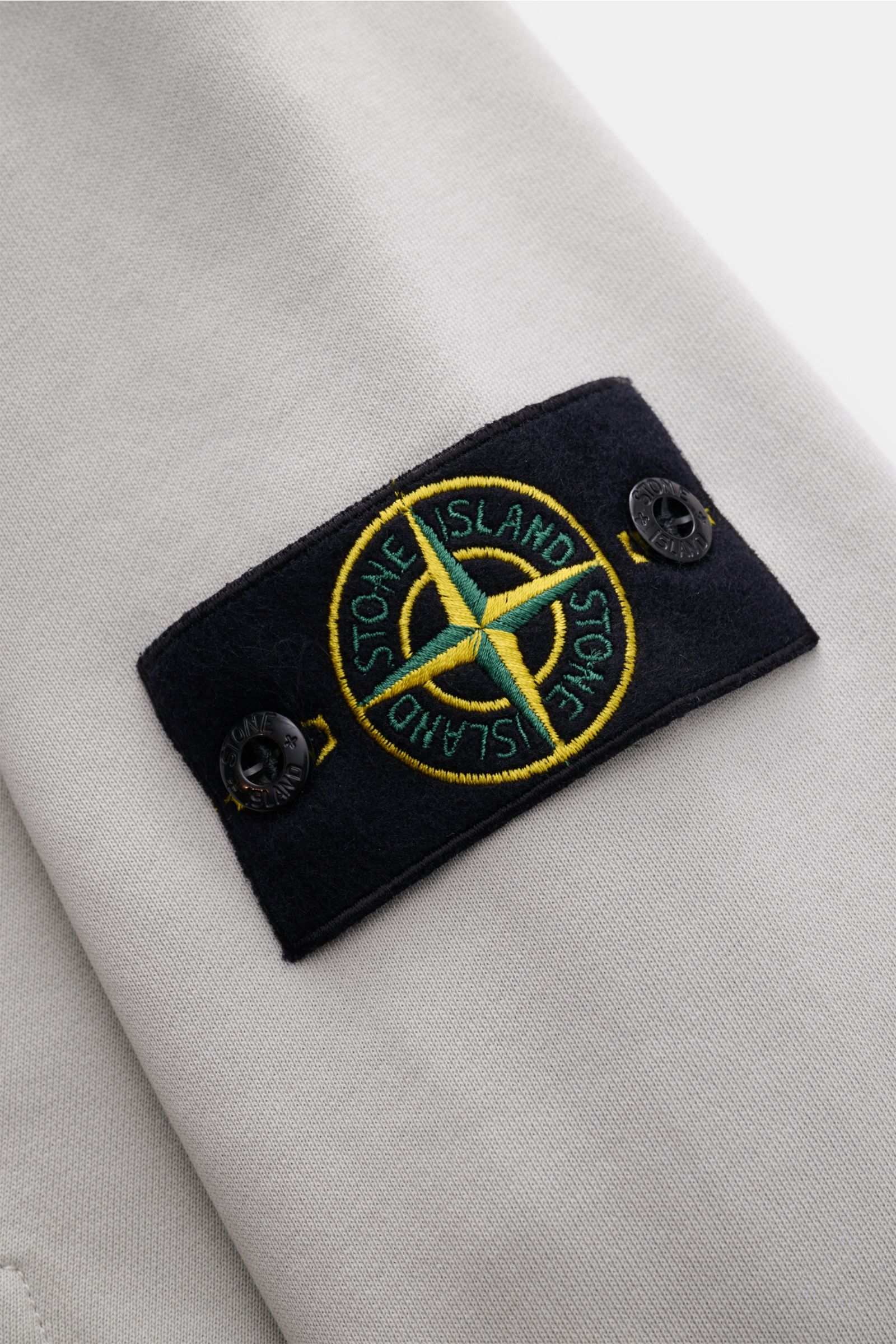 Stone Island Sweatjacke hellgrau im Detail, Nahaufnahme des typischen Kompass-Badge aus softer, stückgefärbter Baumwolle.
