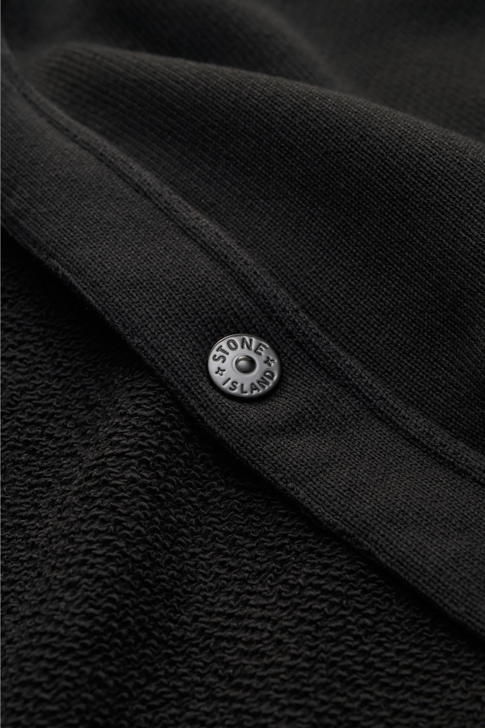 Nahaufnahme des Stone Island Sweat-Cardigan 'Ghost Piece' schwarz aus reiner Baumwolle mit Druckknopf und tonalem Kompass-Badge.