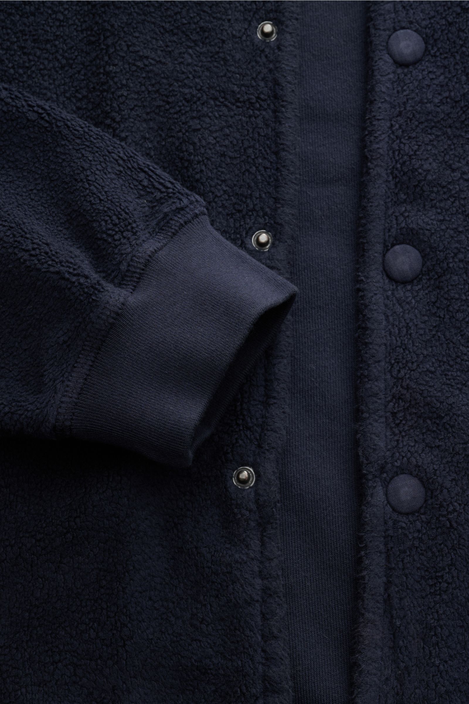 Nahaufnahme des 04651/ A trip in a bag Fleece-Blouson navy von vorne, Slim Fit, reine Baumwolle, weicher Griff, Druckknopfleiste, Blousonkragen, schräge Hüfttaschen, Rippbündchen, Weblabel.