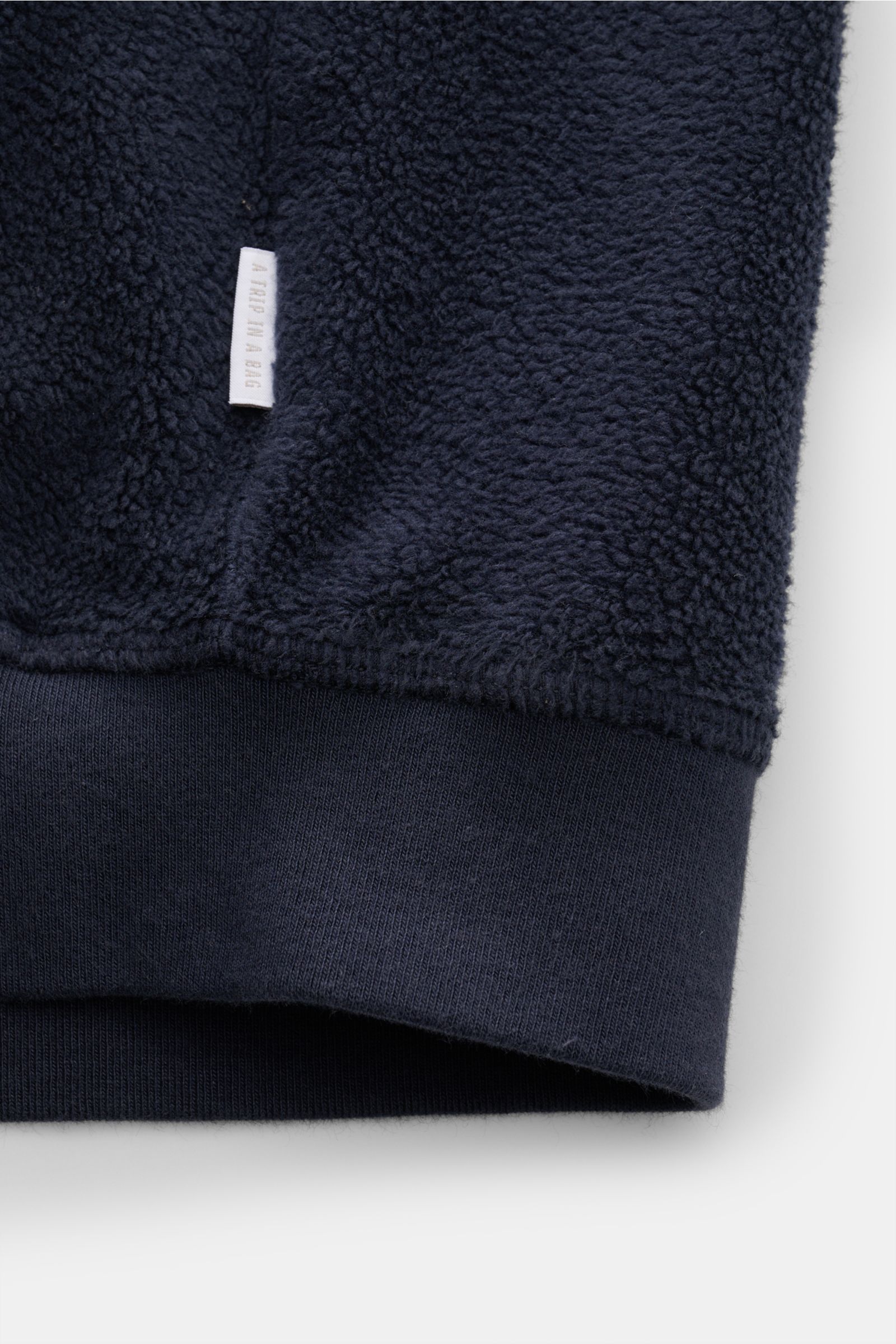 Nahaufnahme des Saums vom 04651/ A trip in a bag Fleece-Blouson navy, Fleece aus reiner Baumwolle, weicher Griff, Slim Fit, Rippbündchen, Weblabel sichtbar.