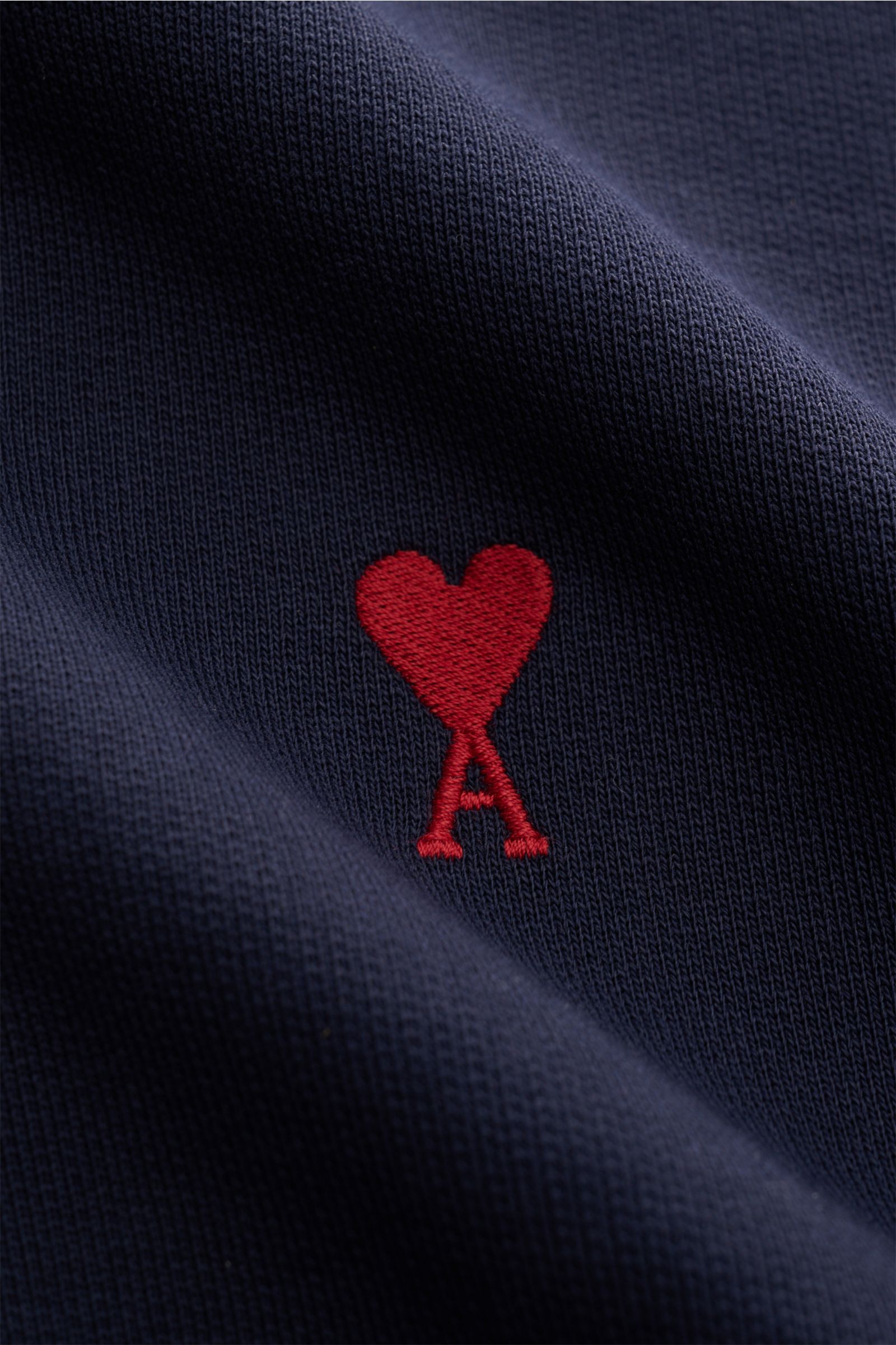 Ami Paris Sweatjacke navy Detailaufnahme aus Nähe, Fokus auf rotes Herz-Stitching auf Bio-Baumwolle mit leicht griffiger Haptik.