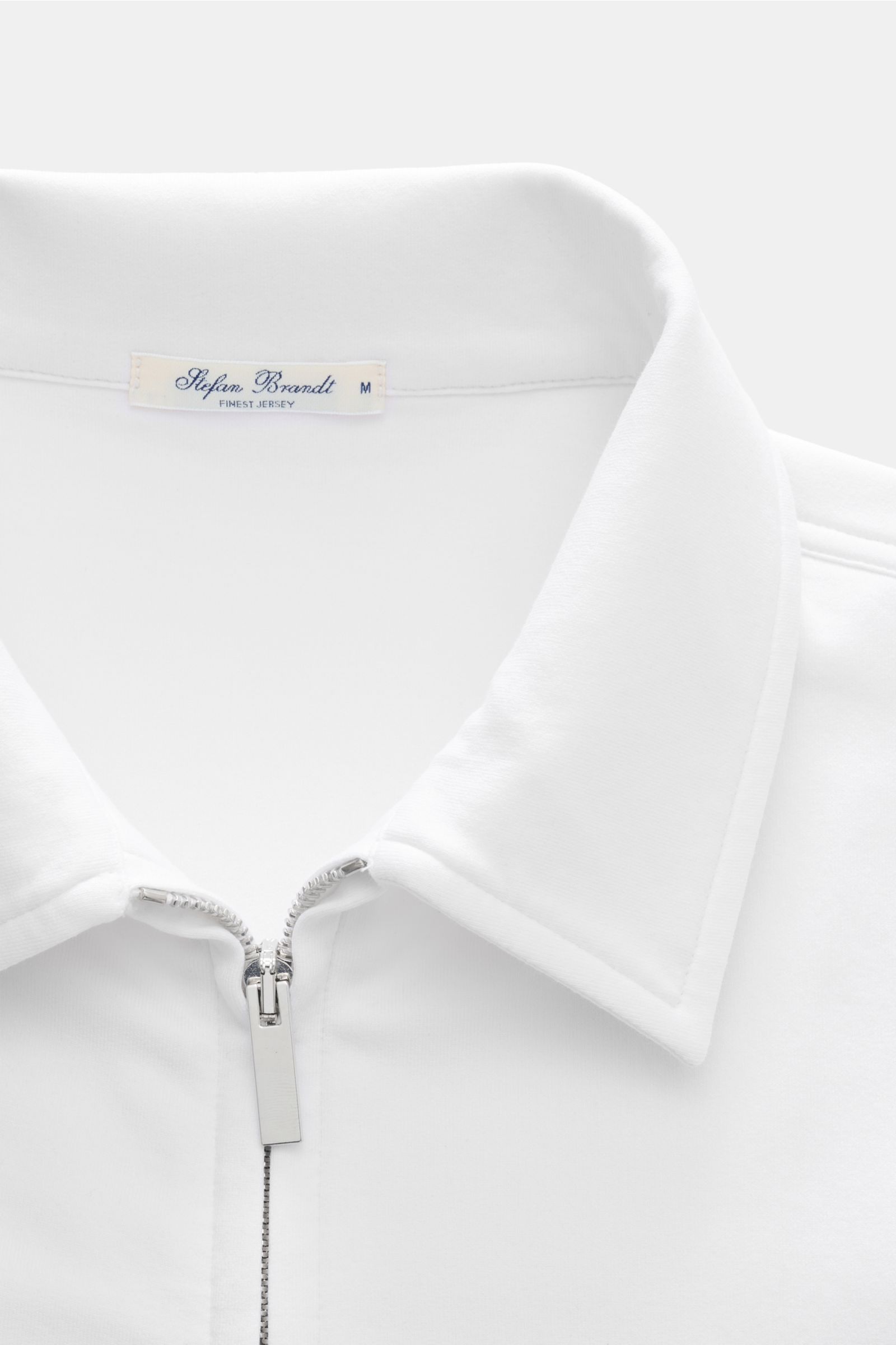Close-up front view of Stefan Brandt Sweatjacke 'Alek' weiß featuring a silver two-way zipper, turn-down collar, and soft white Pima cotton fabric. Spürbarer Komfort auf höchstem Niveau: Selbst ein Essential wie die Sweatjacke 'Alek' wird bei STEFAN BRAND
