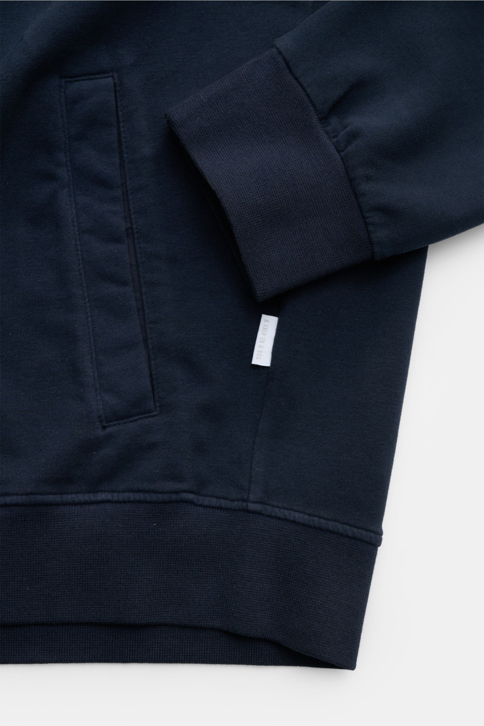 04651/ A trip in a bag Sweatjacke 'IF Track' navy, Detailaufnahme von Ärmel und Tasche, Baumwoll-Jersey, elastisch, garment-dyed, Rippbündchen, Weblabel.