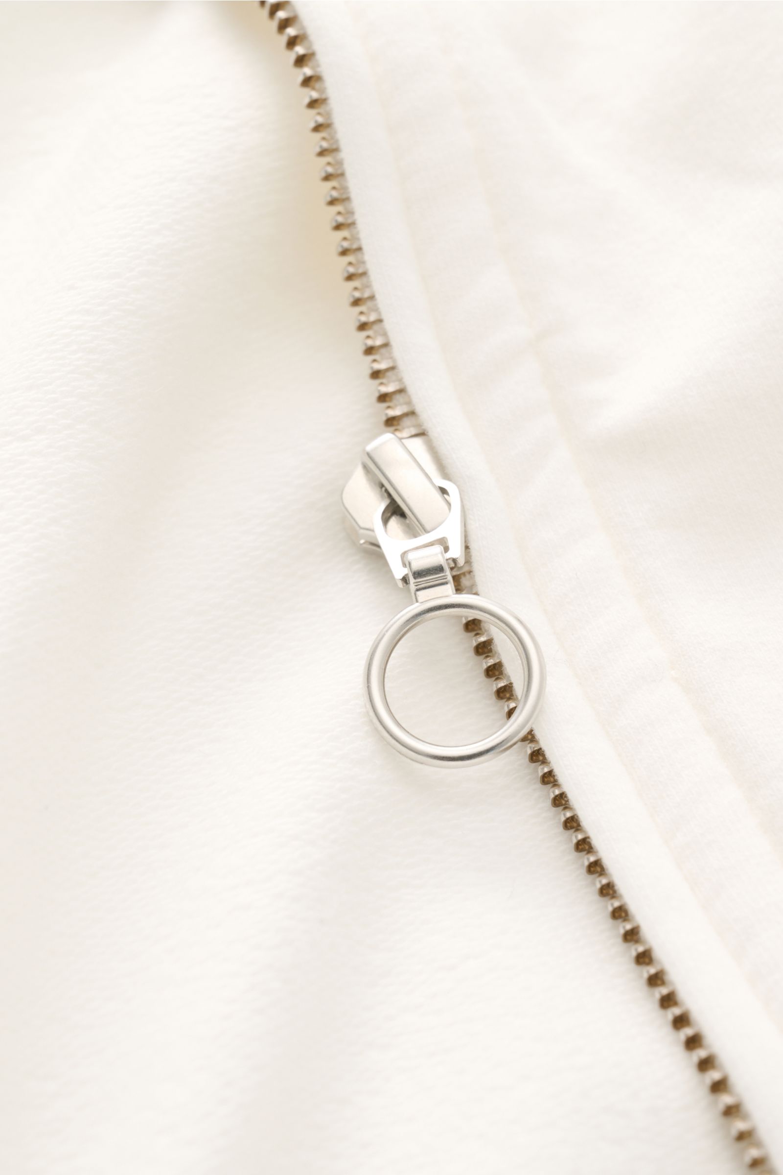 Close-up front view of the silver ring zipper pull on the 04651/ A trip in a bag Sweat jacket 'IF Track' off-white made of soft cotton jersey fabric. 

Relaxation on the move: The sweat jacket 'IF Track' by 04651/ A TRIP IN A BAG is made of super soft 