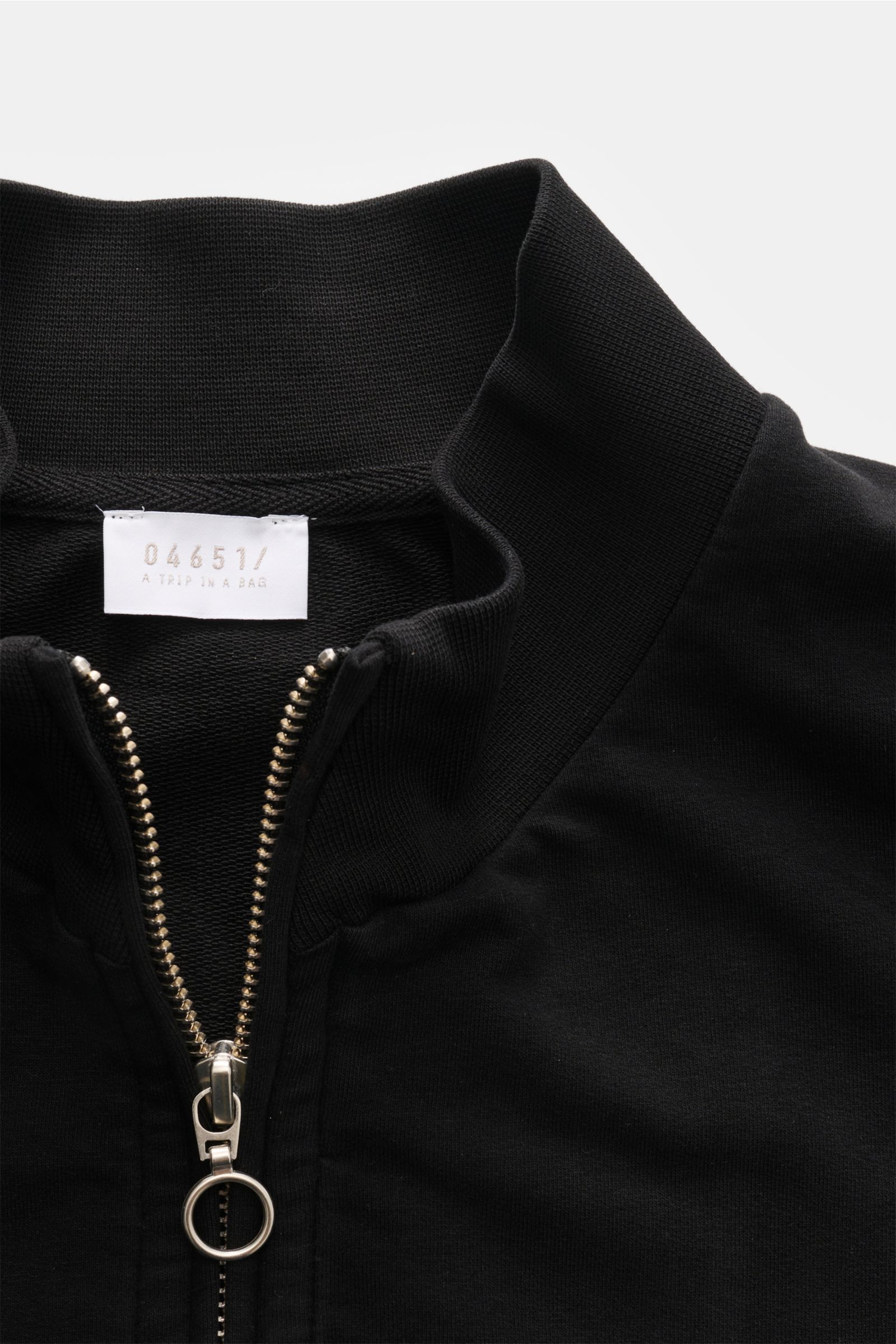 Close-up front view of 04651/ A trip in a bag Sweat jacket 'IF Track' black with high collar, silver zip, and soft cotton jersey fabric.

Relaxation on the move: The sweat jacket 'IF Track' by 04651/ A TRIP IN A BAG is made of super soft cotton jersey 