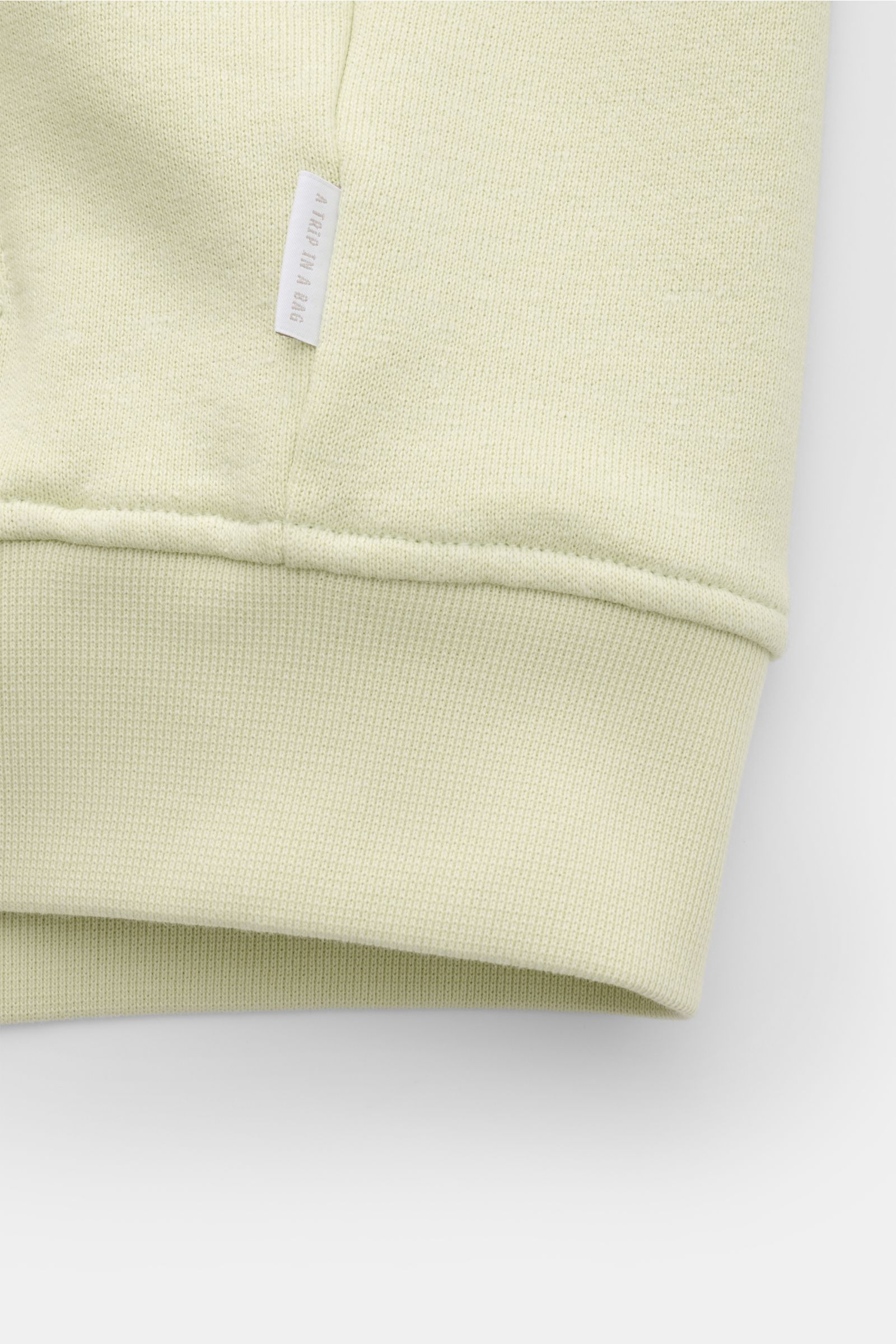 Nahaufnahme der pastellgrünen 04651/ A trip in a bag Sweatjacke 'CL Bomber' mit weichem Griff, flexiblem Rippbündchen und kleinem Weblabel.