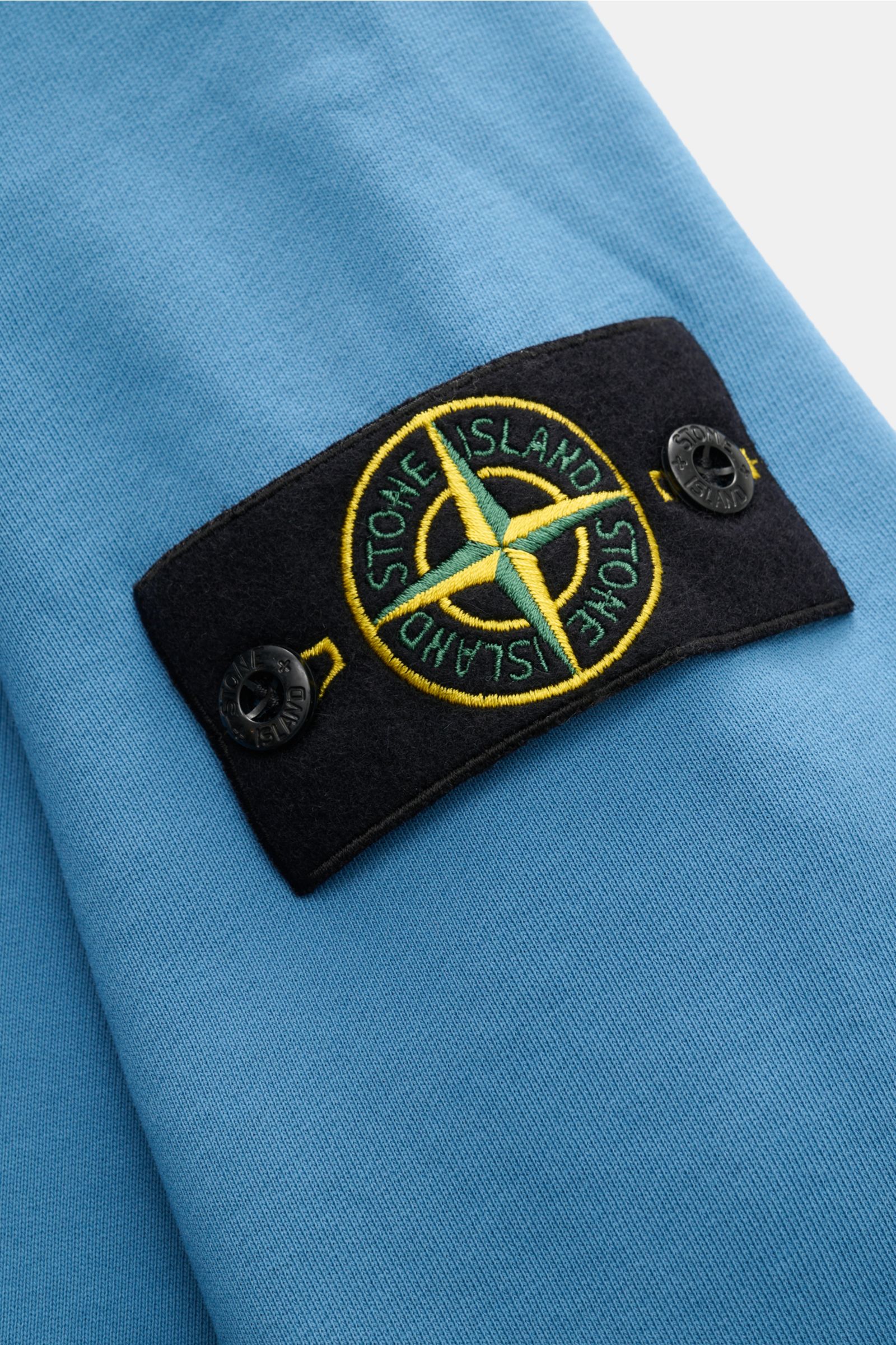 Stone Island Kapuzenpullover blau, Nahaufnahme Ärmel mit typischem Kompass-Badge, Sweat aus reiner Baumwolle, weicher Griff, garment dyed, Regular Fit, markante Overlock-Nähte, Kapuze mit Tunnelzug, Kängurutasche, komfortable Rippbündchen.