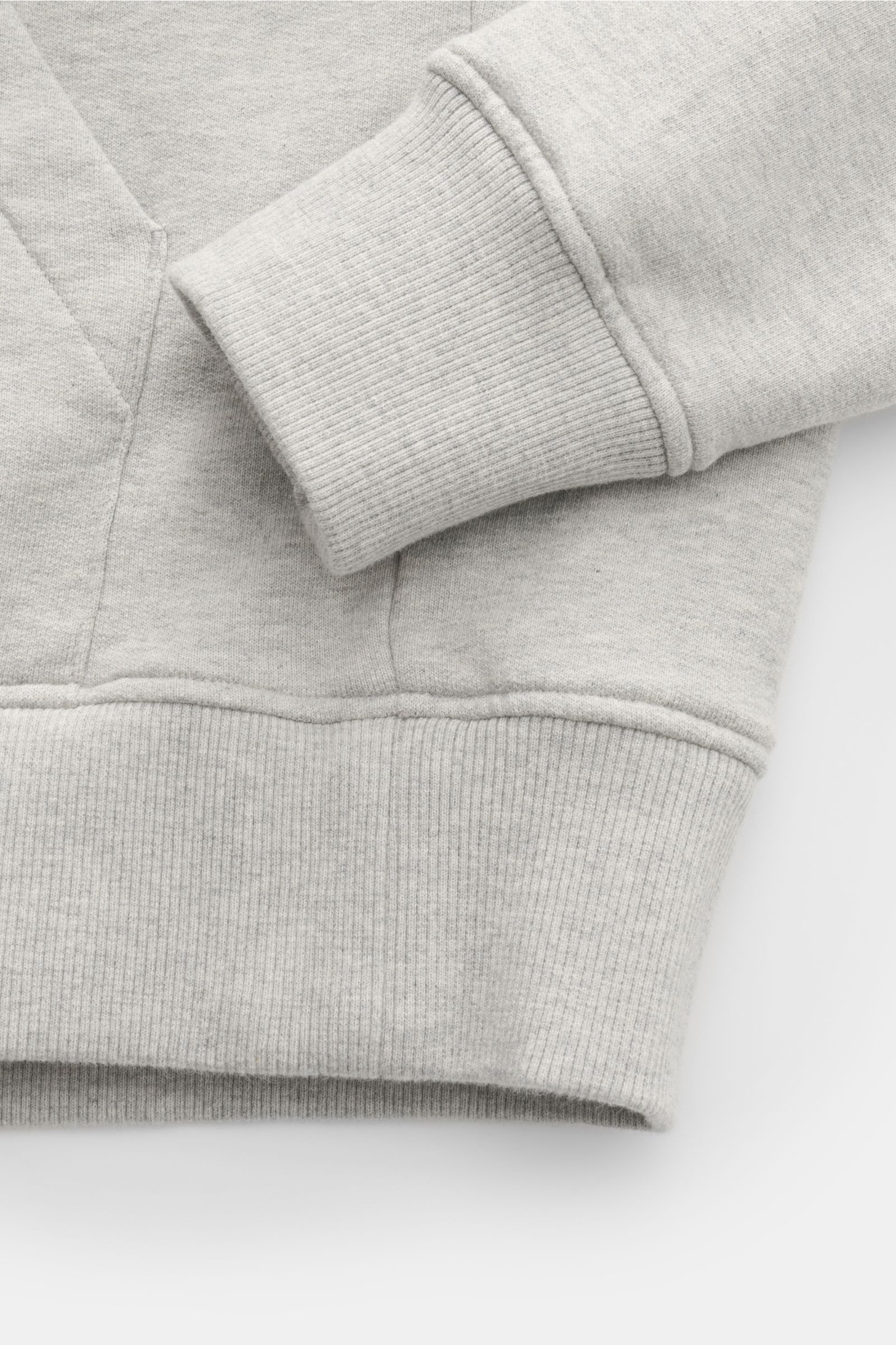 Nahaufnahme des Ami Paris Kapuzenpullovers grau meliert von unten, zeigt elastische Baumwolle, Kängurutasche, Rippbündchen und Herz-Stitching.