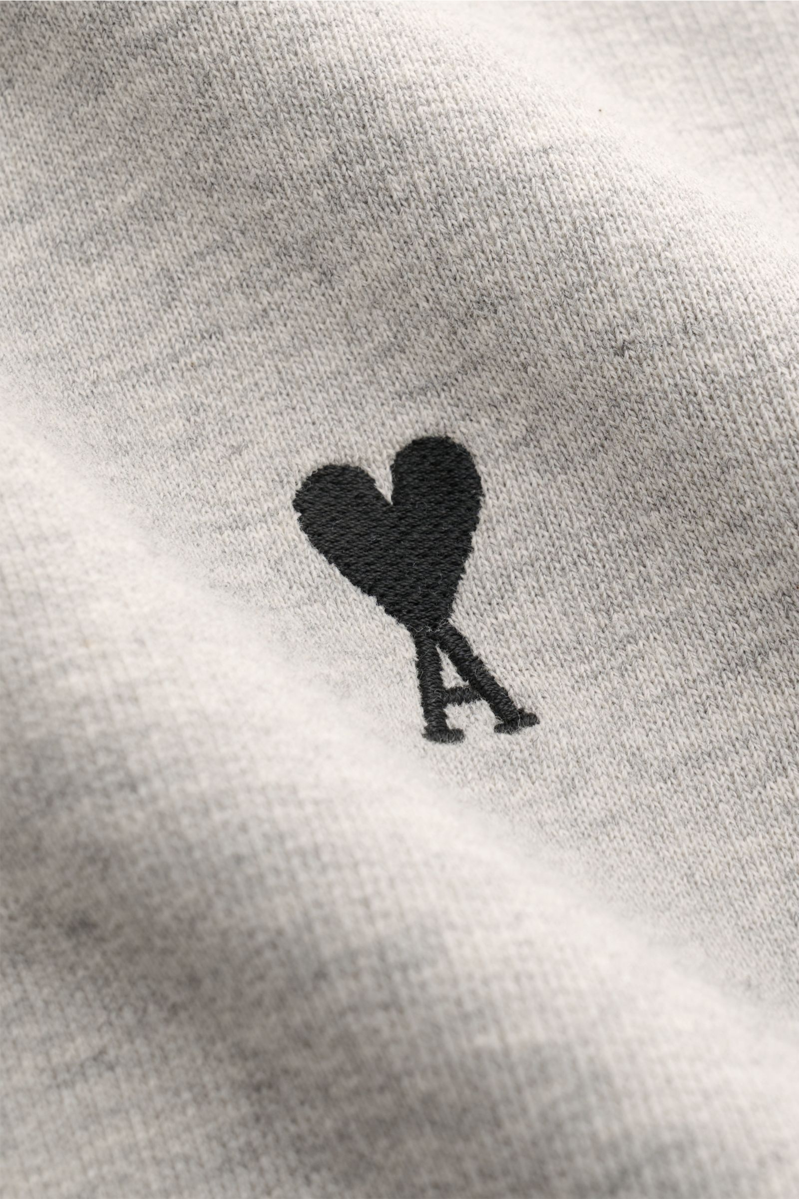 Nahaufnahme der Ami Paris Sweatjacke hellgrau meliert mit dezent gesticktem schwarzen Herz-Stitching auf der Brust aus Baumwolle.