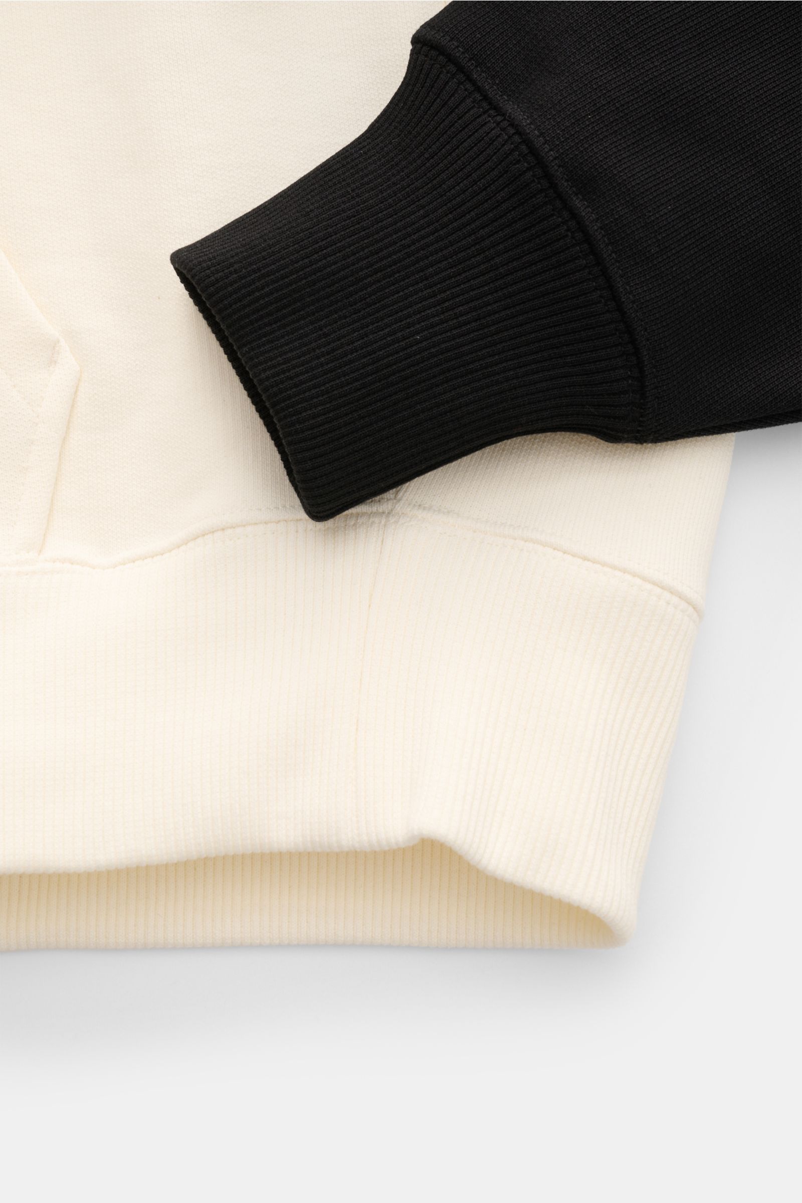 Nahaufnahme des Saum- und Ärmelbündchens des Ami Paris Kapuzenpullovers 'Boxy Fit' creme/schwarz mit Raglanärmel, Kängurutasche, Kapuze und flexiblem Rippbündchen aus reiner Baumwolle.