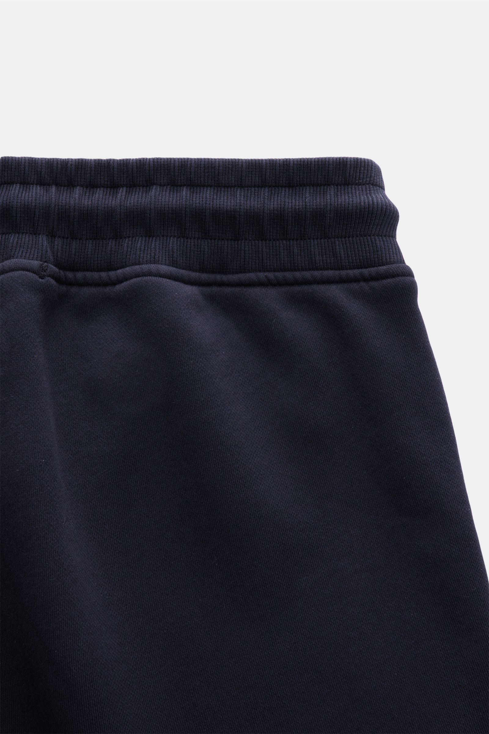 C.P. Company Cargo-Sweathose dark navy in Slim Fit, kurze, schmal zulaufende Sweathose aus weicher Baumwolle mit elastischem Bund, Tunnelzug, Rippbündchen, Cargo-Tasche mit Linsen-Detail, Seitennahttaschen, aufgenommen aus Nahaufnahme der oberen Bundparti