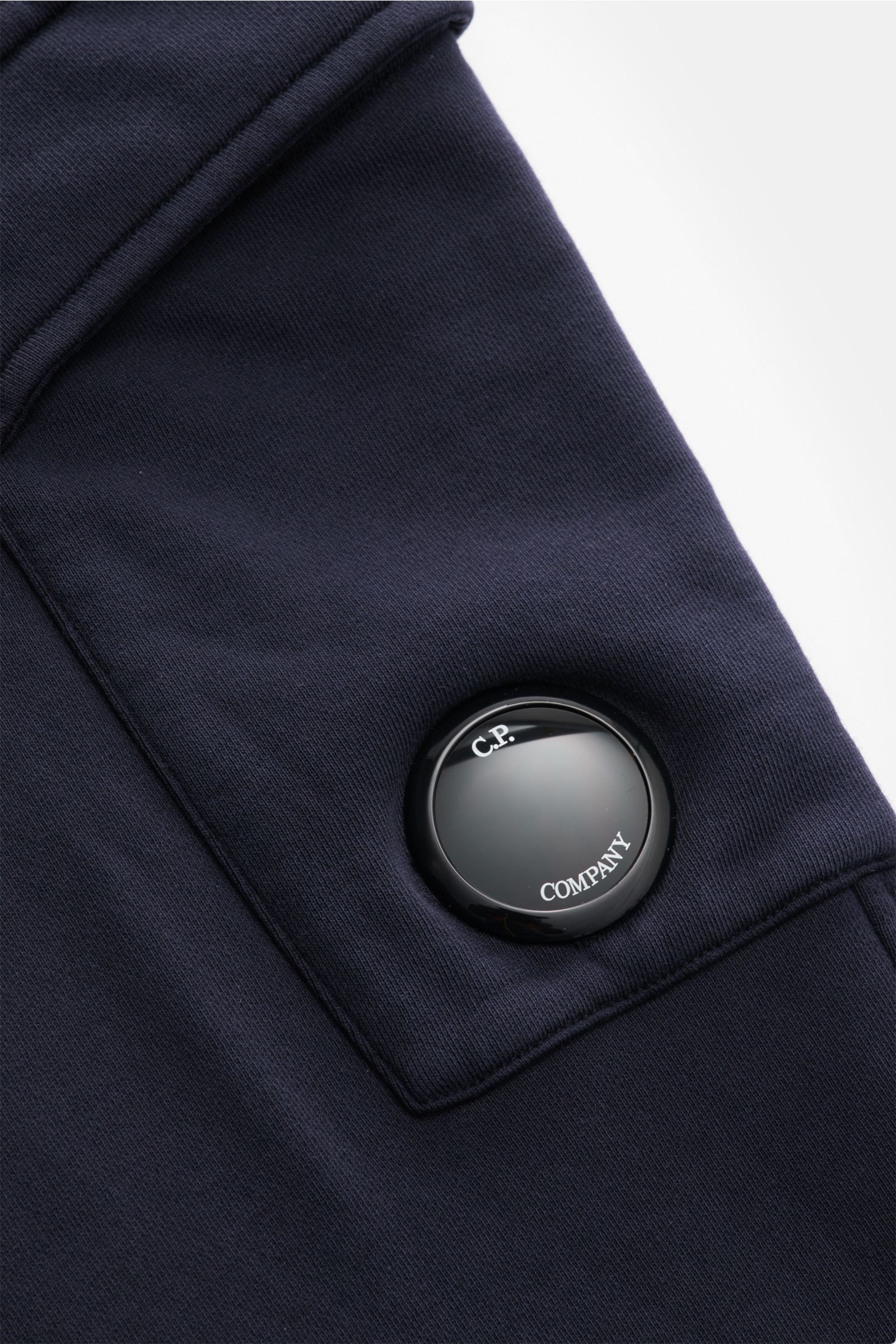 Nahaufnahme der C.P. Company Cargo-Sweathose dark navy aus Baumwolle, Fokus auf Cargo-Tasche mit Linsen-Detail und feiner Naht.