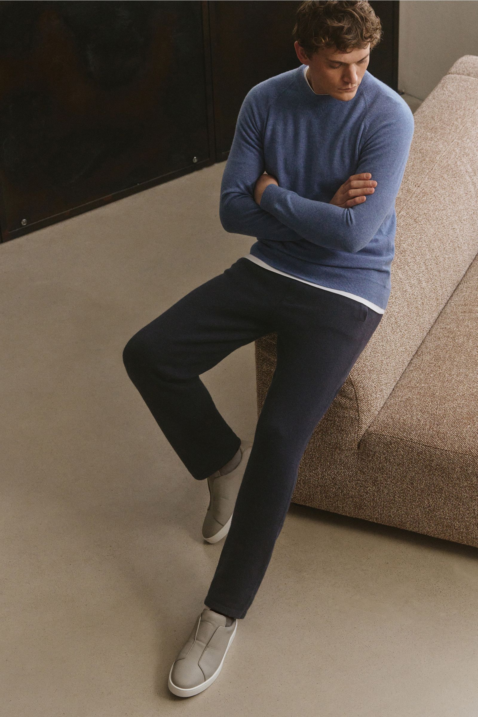 Mann sitzt seitlich auf Sofa, trägt von Braun Cashmere Jogpants navy mit geradem Schnitt, elastischem Bund, schrägen Taschen, aus mongolischem Cashmere.