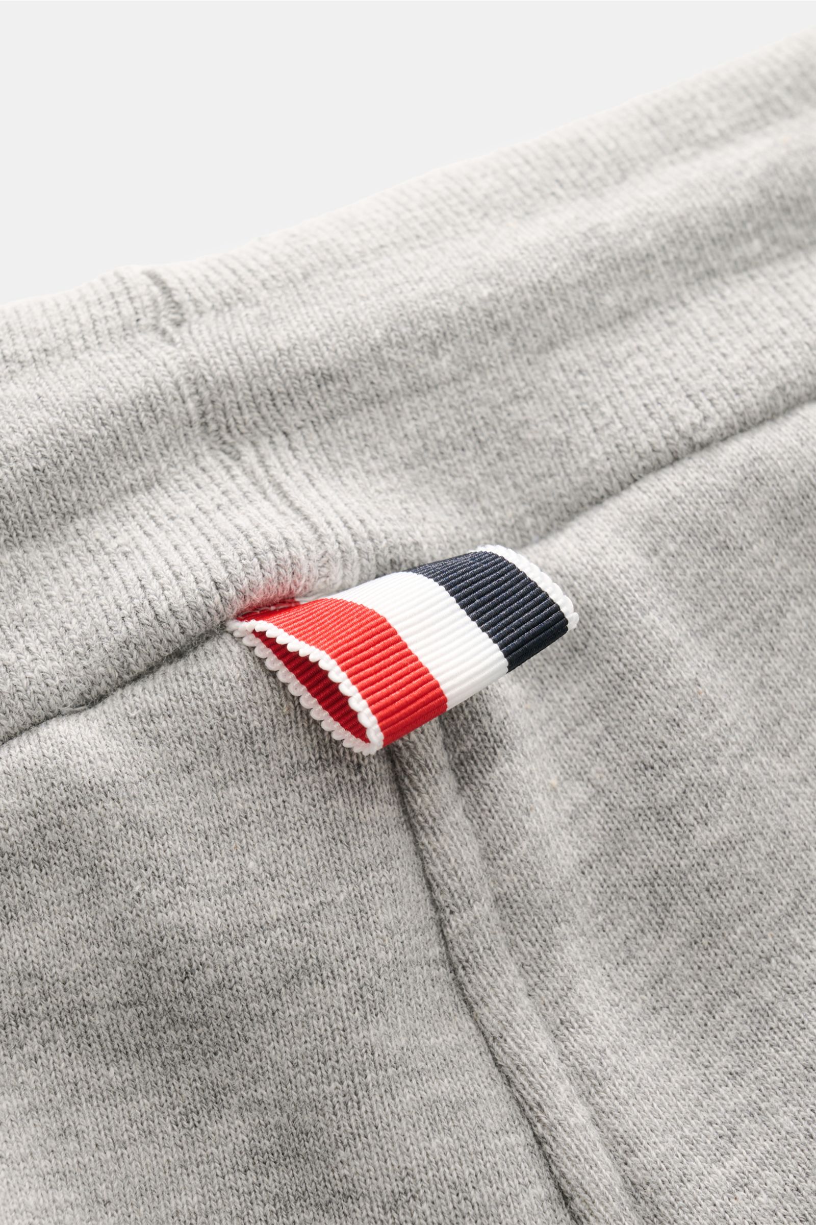 Nahaufnahme der grau melierten Thom Browne Sweathose mit elastischem Bund und markentypischem Streifen-Detail, weicher Baumwollstoff.