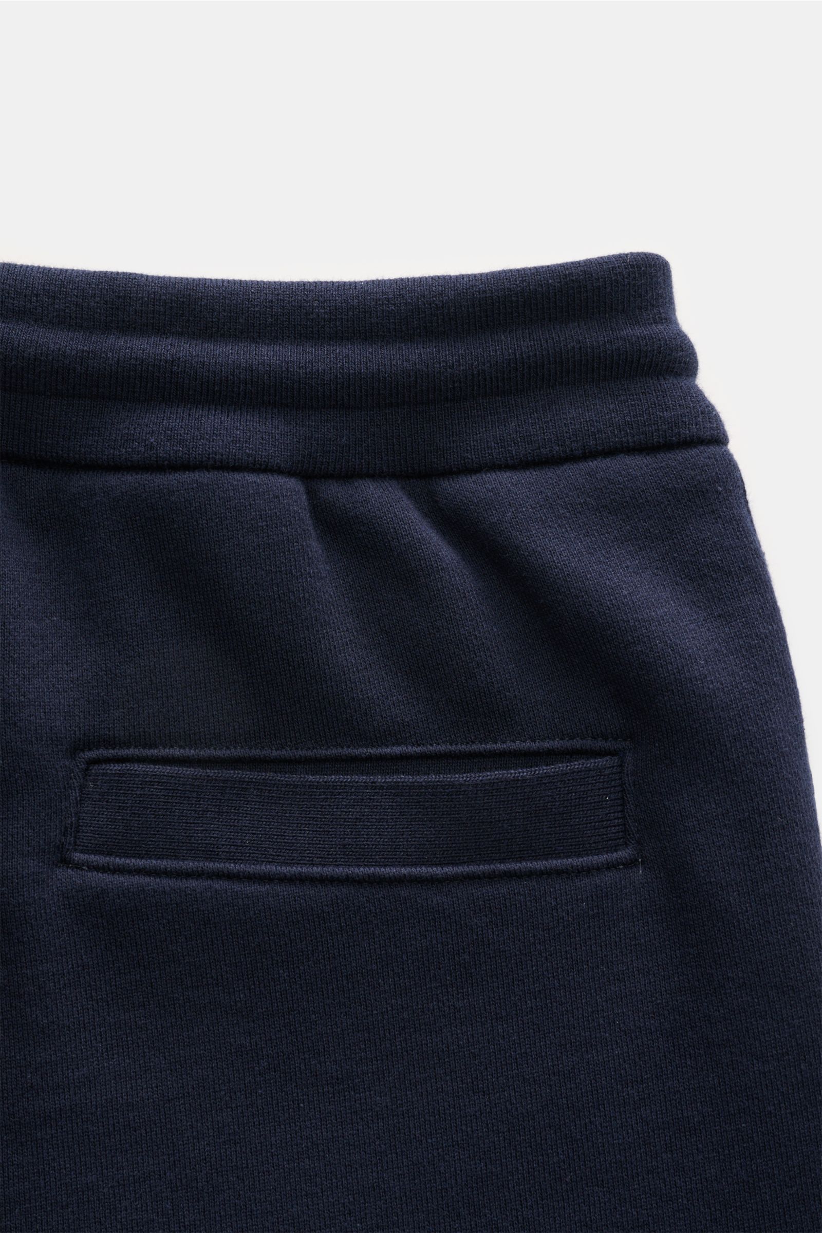Nahaufnahme der Thom Browne Sweathose navy aus reiner Baumwolle, weicher Griff, elastischer Bund mit Tunnelzug, schmal zulaufend, mit Rückentasche, frontal fotografiert.