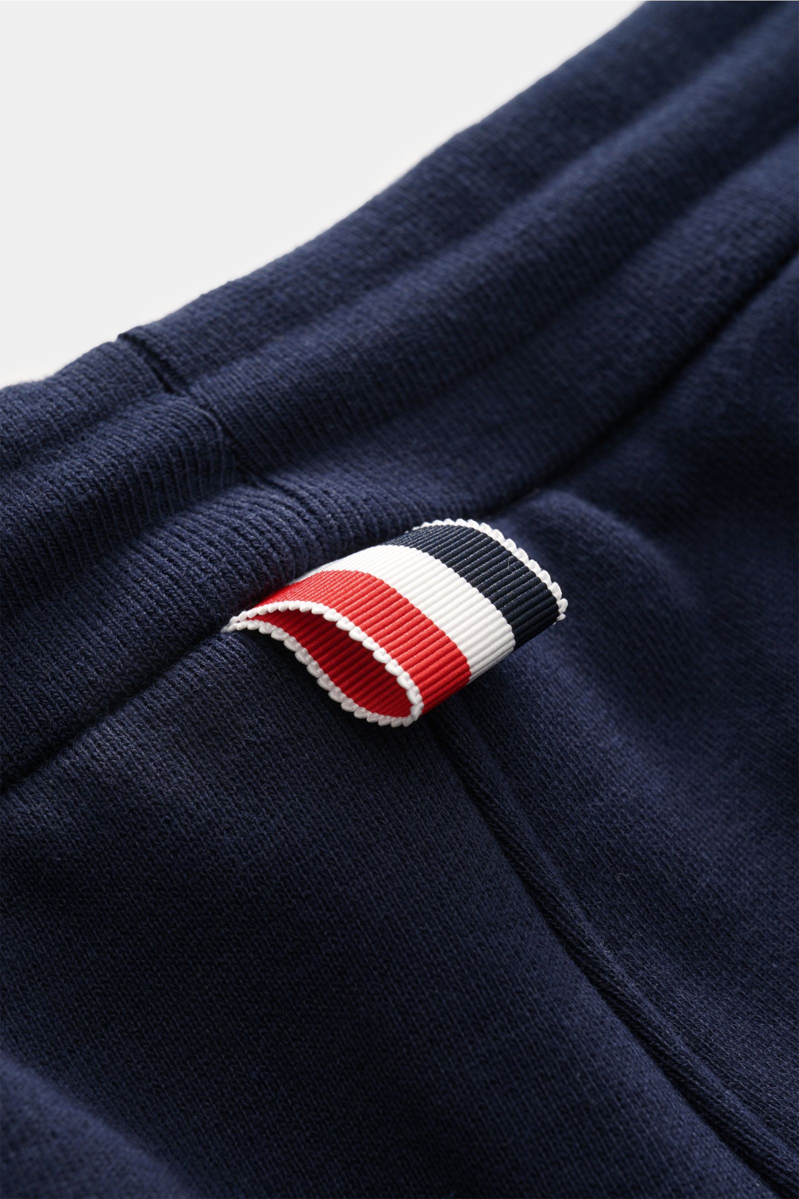 Nahaufnahme der Thom Browne Sweathose navy aus reiner Baumwolle, slim fit mit elastischem Bund und markentypischem Streifen-Detail, seitlich fotografiert.