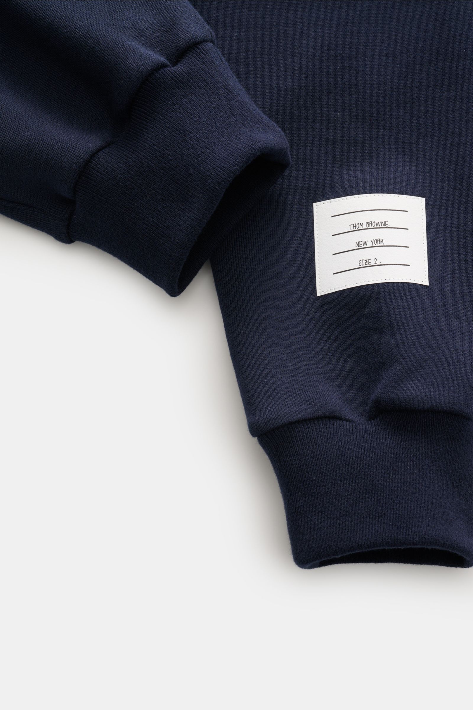 Thom Browne Sweathose navy in Nahaufnahme von oben, weicher Baumwollstoff mit Rippbündchen und weißem Markenlabel sichtbar.