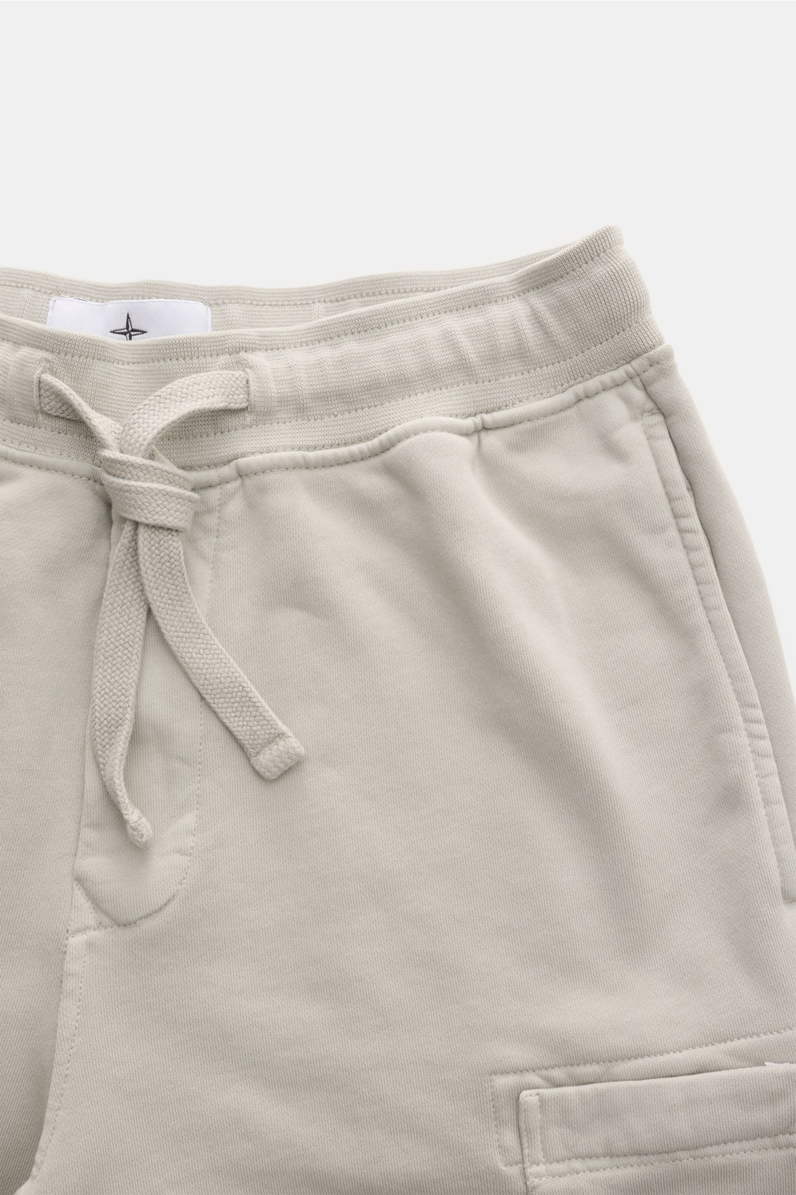 Stone Island Sweatshorts 'Felpa Bermuda' hellgrau, von oben fotografiert, aus reiner Baumwolle mit elastischem Bund, Tunnelzug, Nahttaschen, Cargo-Tasche, Kompass-Badge und Gesäßtasche mit Druckknopf.