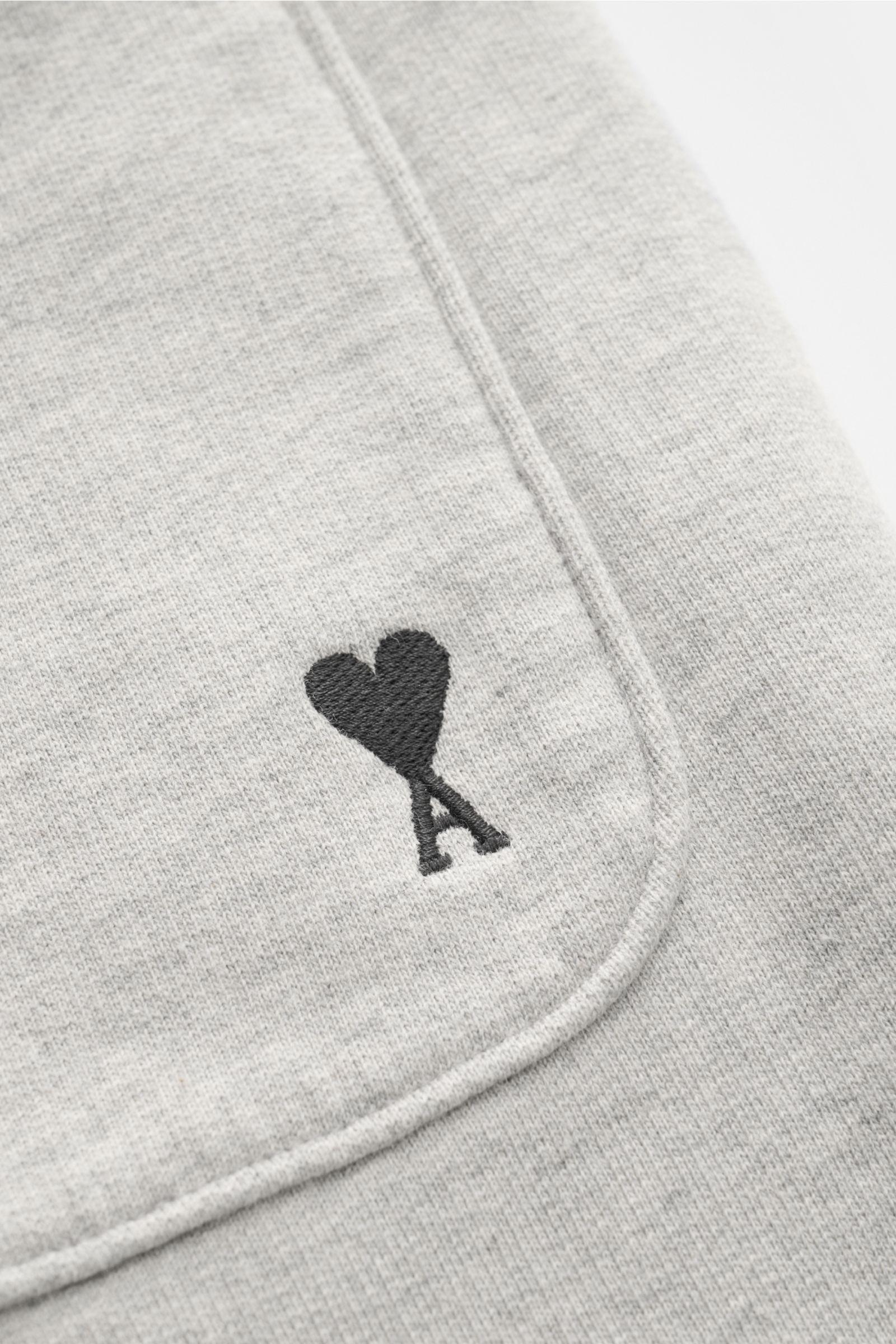 Close-up front-side view of Ami Paris Sweat-Bermudas 'Quota' grau meliert showing soft elastic cotton fabric, side seam pocket, elastic waistband with drawstring, and black heart logo stitching on the back pocket. Lässig durch die warme Saison: Die 'Quota