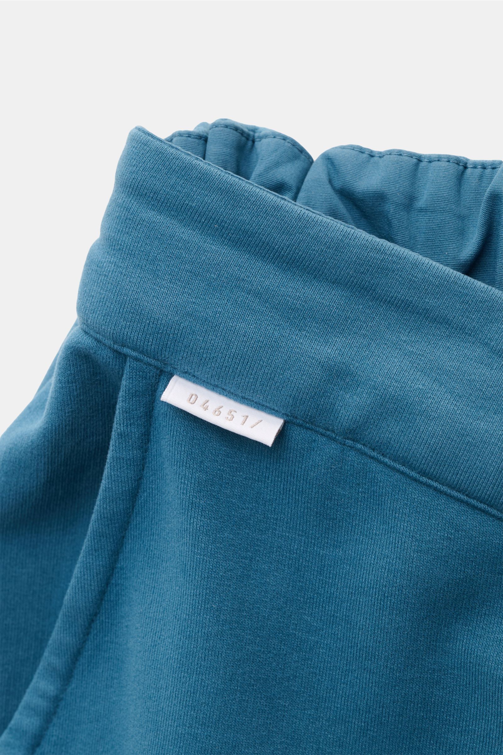 Nahaufnahme der elastischen Bündchenpartie der petrolfarbenen 04651/ A trip in a bag Sweat-Shorts aus weichem Baumwoll-Sweat mit kleinem Weblabel.