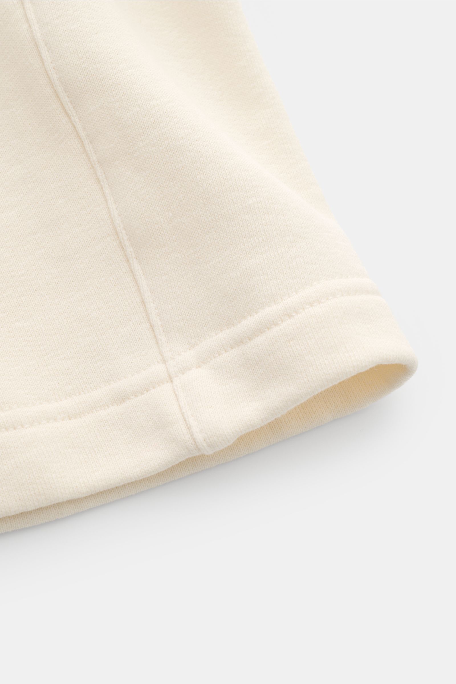 Nahaufnahme der cremefarbenen 04651/ A trip in a bag Sweat-Shorts 'CL' aus Bio-Baumwolle und Leinen mit weichem Griff, sichtbarer Naht und Saum, fotografiert von schräg oben.