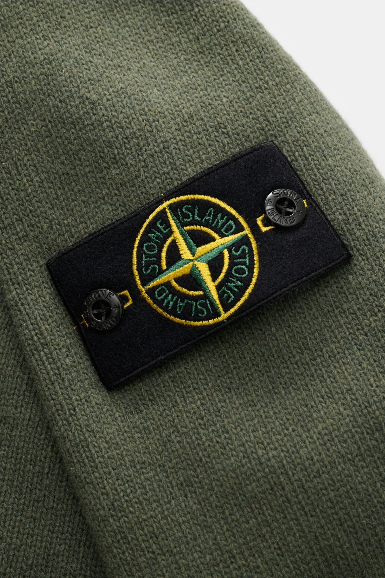 Nahaufnahme des markentypischen Kompass-Badges am Oberarm des Stone Island Troyer 'Lambswool' oliv aus wärmendem Wollmix.