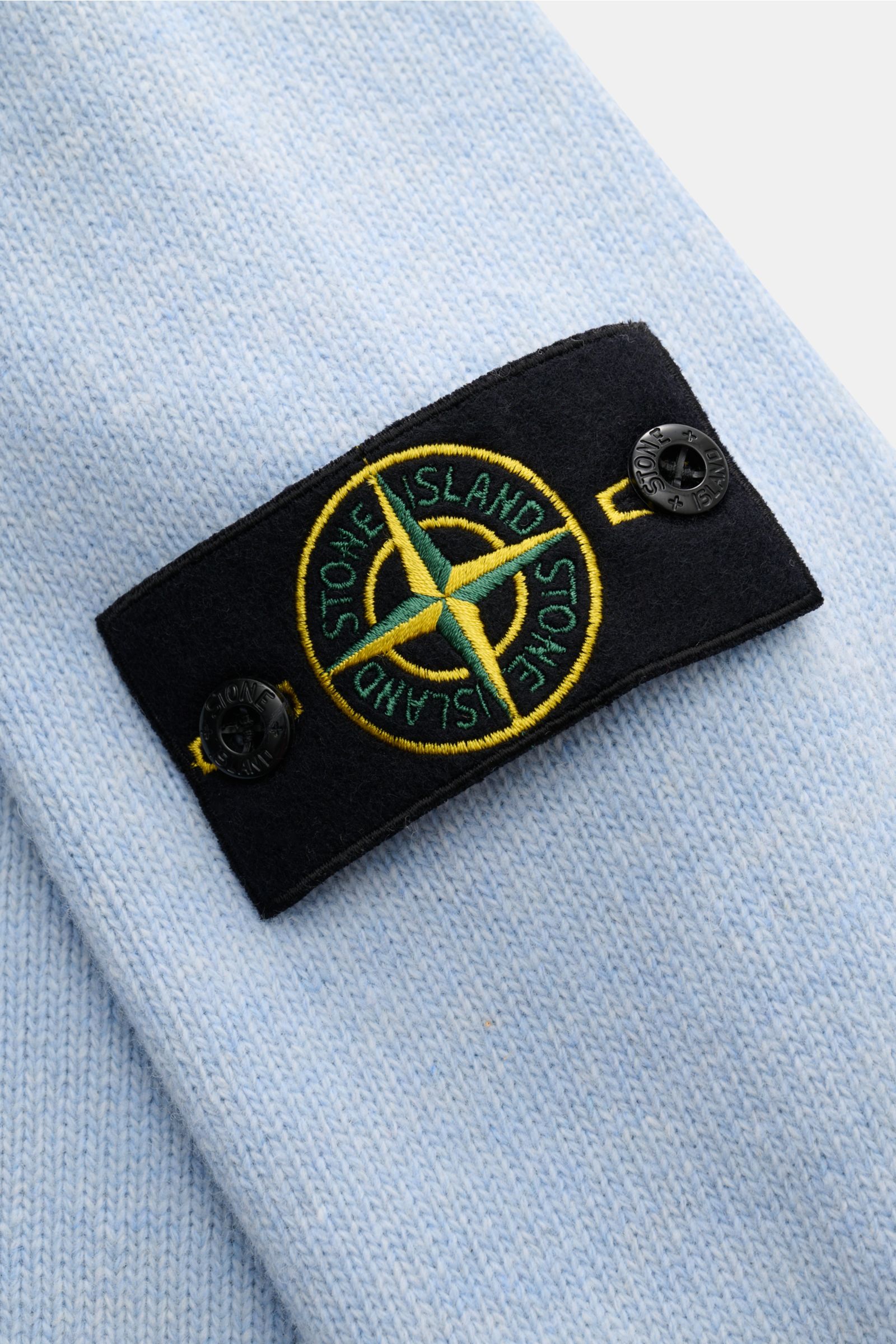Close-up of the black compass badge with yellow and green embroidery on the light blue Stone Island Half-zip jumper 'Lambswool' light blue, showing the wool blend knit texture from a top-down perspective. A stylish essential for the colder months: This