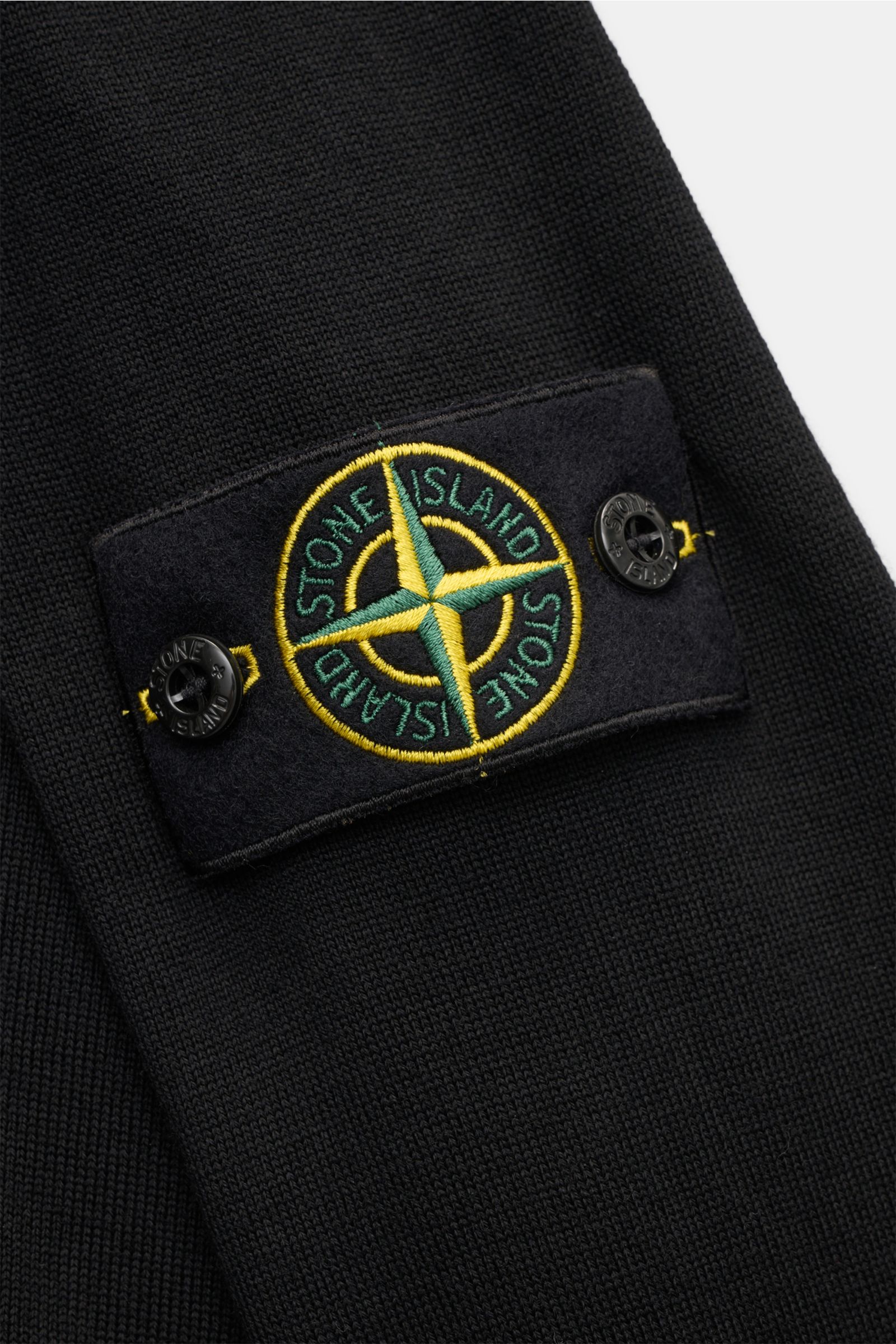 Close-up view of the sleeve of the Stone Island Troyer 'Light Pure Wool' schwarz, showcasing the black fine wool knit and the iconic compass badge with buttons.

Ein Strickklassiker mit zeitloser Ausstrahlung: Dieser Troyer von STONE ISLAND steht mit f
