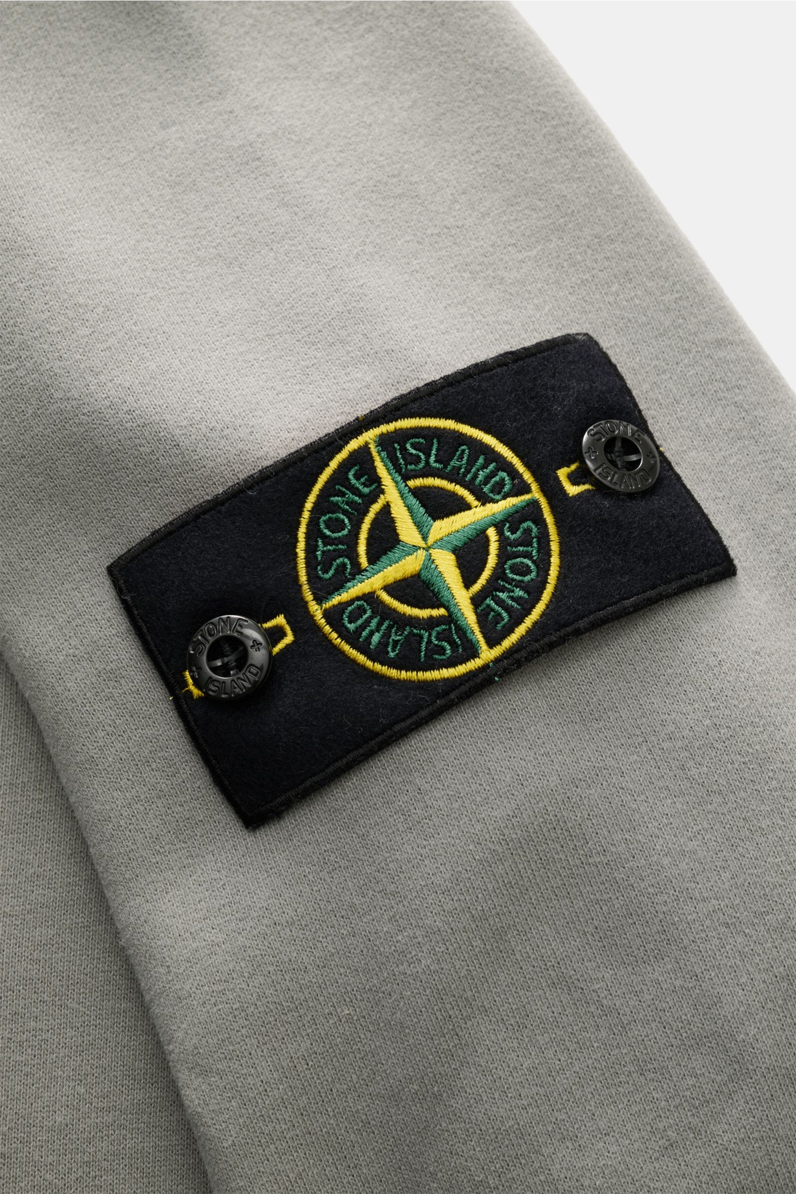 Nahaufnahme des markentypischen Kompass-Badges am Ärmel des Stone Island Sweat-Troyer grau aus weicher Baumwolle.
