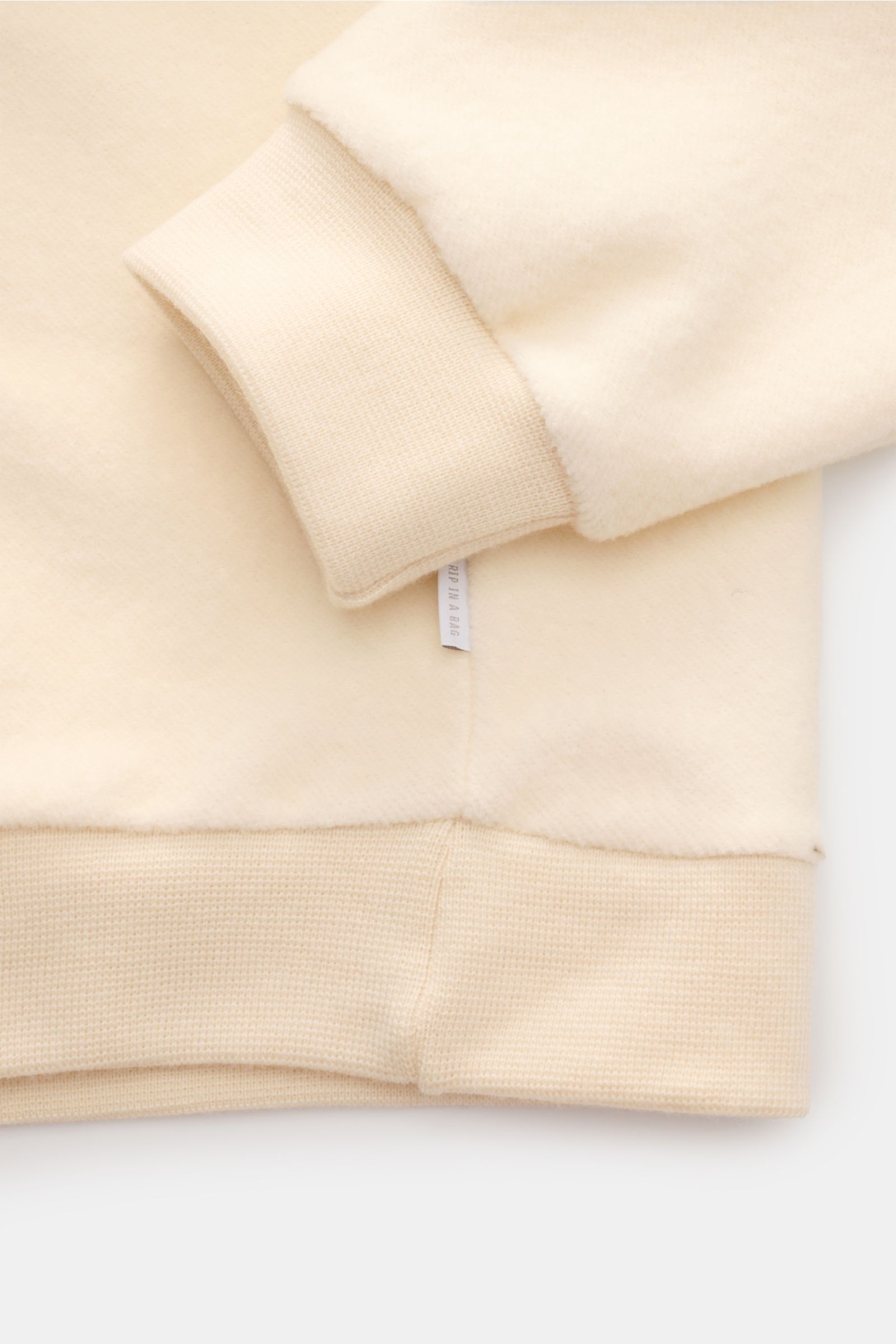 Close-up side view of the 04651/ A trip in a bag Troyer 'Cw Quarter Zip' creme showing soft fleece texture, ribbed cuffs, hem, and side seam weblabel. Lässig durch die Übergangszeit: Der Troyer von 04651/ A TRIP IN A BAG überzeugt mit seiner samtigen Flee
