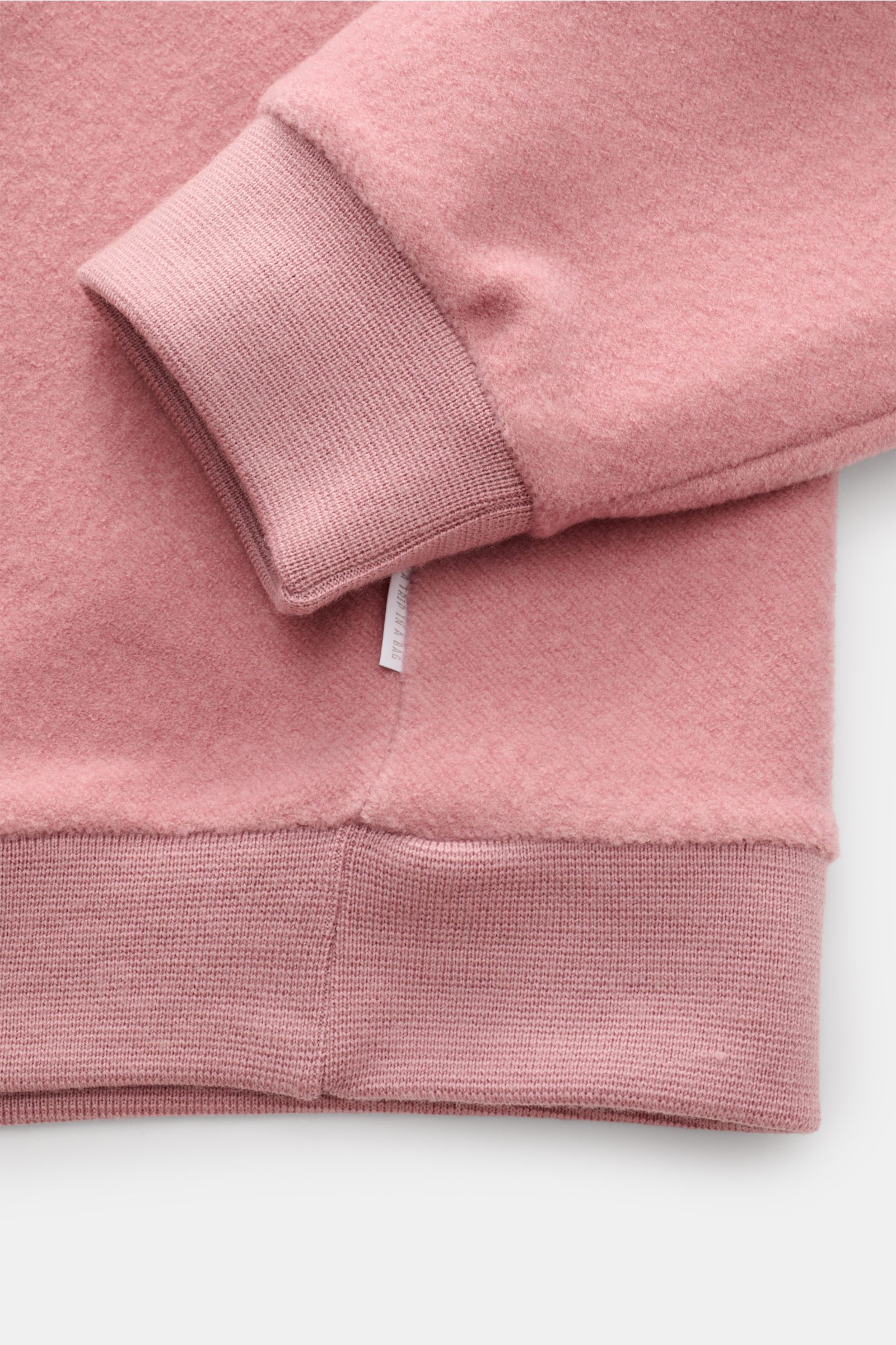 Close-up view of the cuff and hem of the 04651/ A trip in a bag Troyer 'Cw Quarter Zip' altrosa in soft pink fleece with ribbed cuffs and hem, showing the doubleface wool-cotton mix texture and side seam weblabel. Lässig durch die Übergangszeit: Der Troye