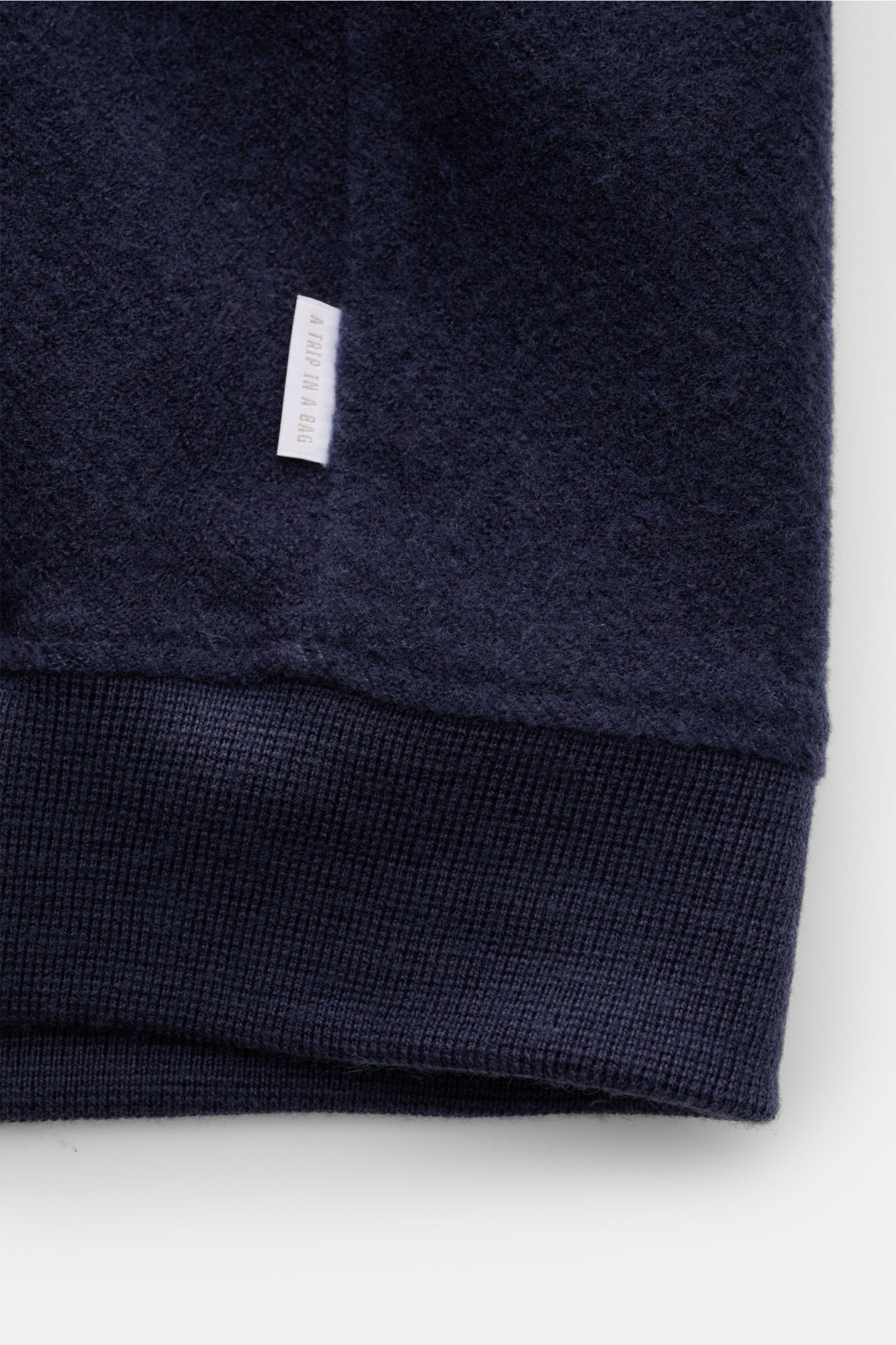 Close-up of the hem of the 04651/ A trip in a bag Blouson dunkelblau, showing its soft wool-cotton fleece texture, ribbed cuffs, and side seam web label, photographed from a front angle.

Description (integrated content): Lässig durch die Übergangszeit: D