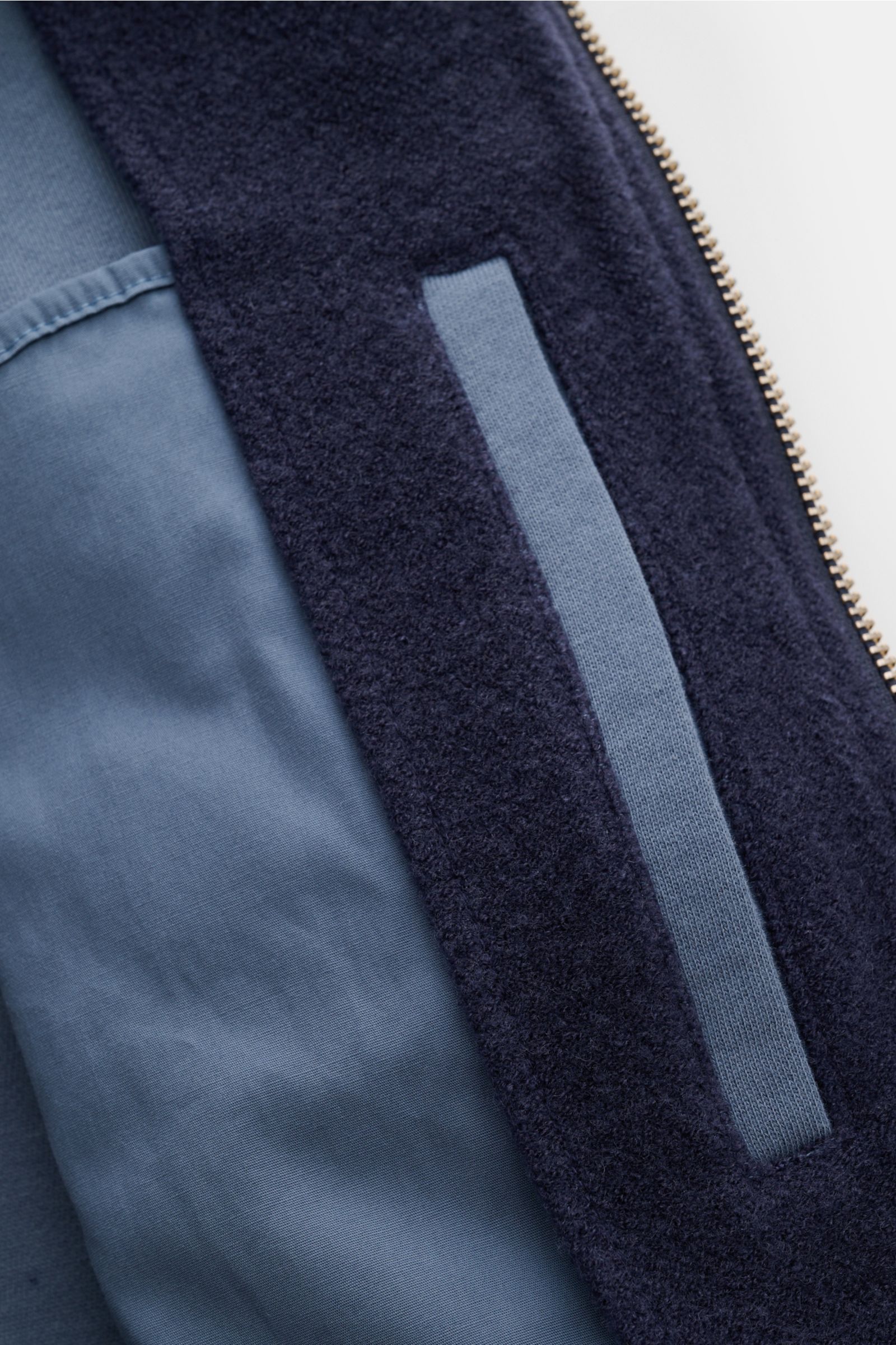 Close-up view of the 04651/ A trip in a bag Blouson dunkelblau showing its soft fleece texture, blue cotton lining, two-way zipper, and rib-knit collar, highlighting wool-cotton blend and slim fit details.

Lässig durch die Übergangszeit: Der Blouson v