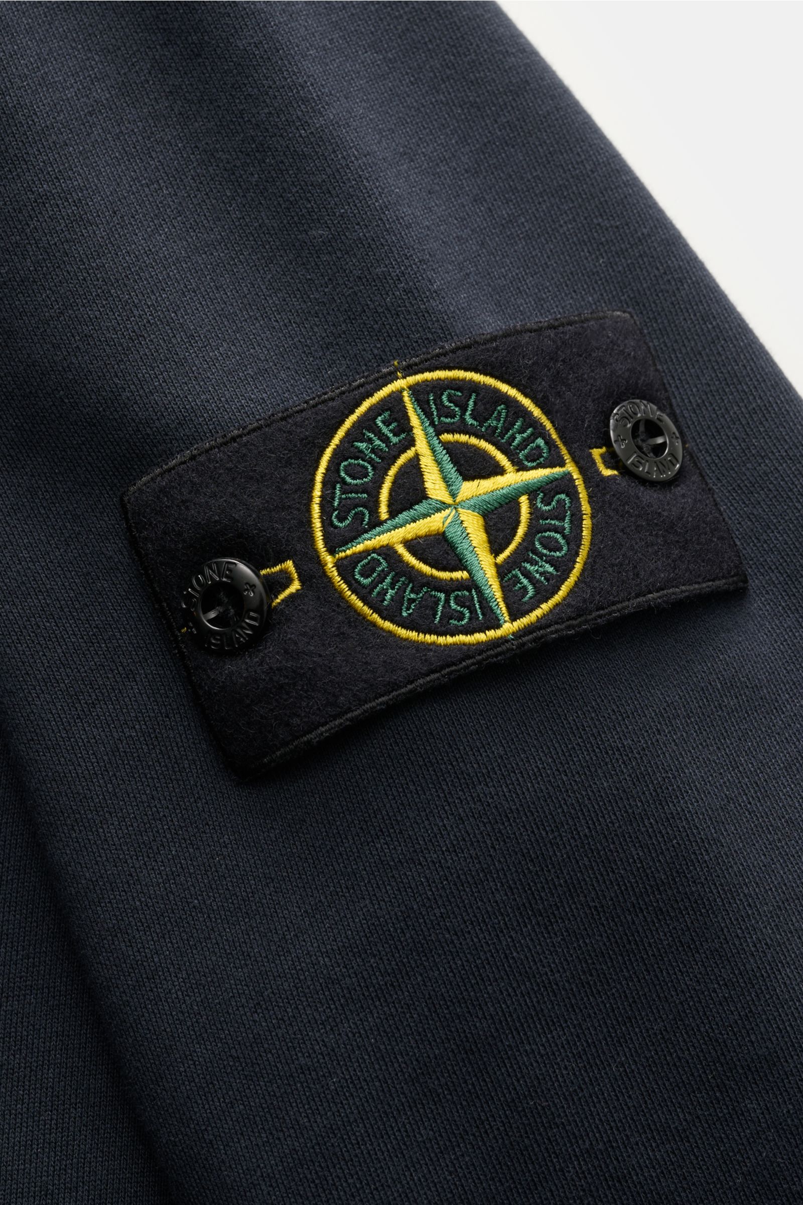 Nahaufnahme des Kompass-Badges am Oberarm des Stone Island Troyer 'Basic Sweat' navy aus reiner Baumwolle mit weicher Qualität, Slim Fit, Troyer-Kragen mit Zipper und elastischen Ärmelbündchen, fotografiert von schräg oben.