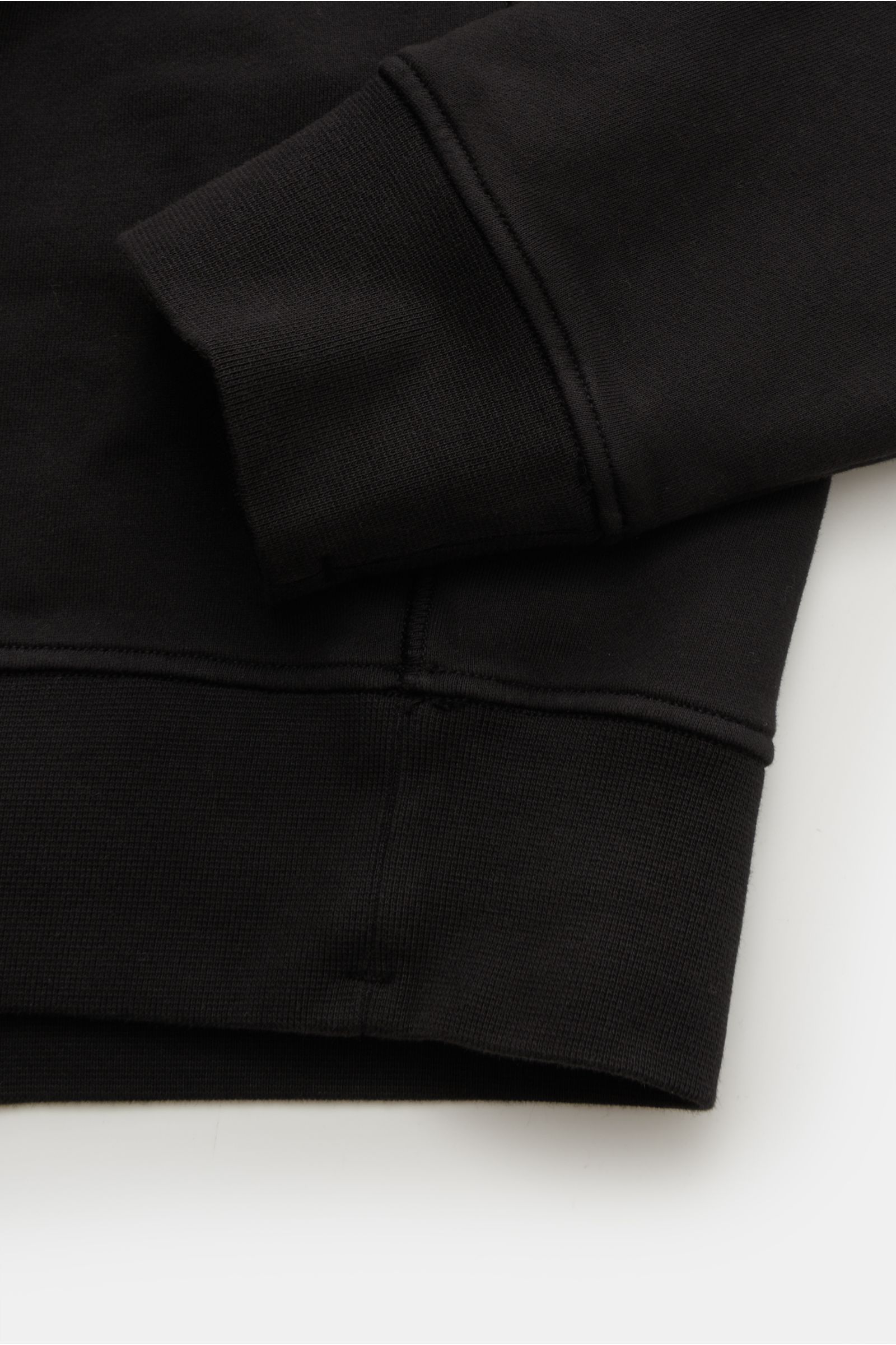 Close-up side view of the cuff and hem of the Stone Island Troyer 'Basic Sweat' schwarz in black cotton fabric with ribbed flexible cuffs.

Description: Sportives Essential: Der Sweat-Troyer von STONE ISLAND überzeugt als legeres Basic Piece und wird z