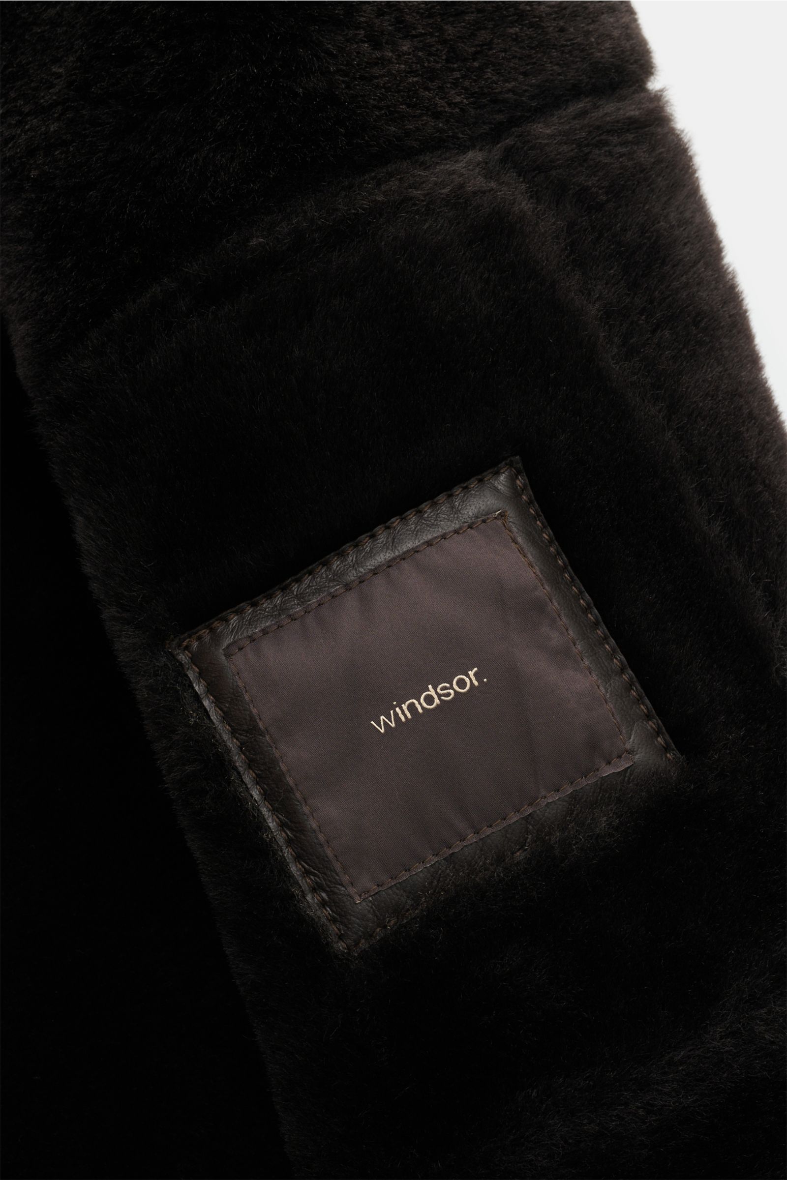 Detailaufnahme der luxuriösen, dunkelbraunen Windsor Lammfelljacke 'Aro' mit weichem Lammfell und Markenlabel innen.