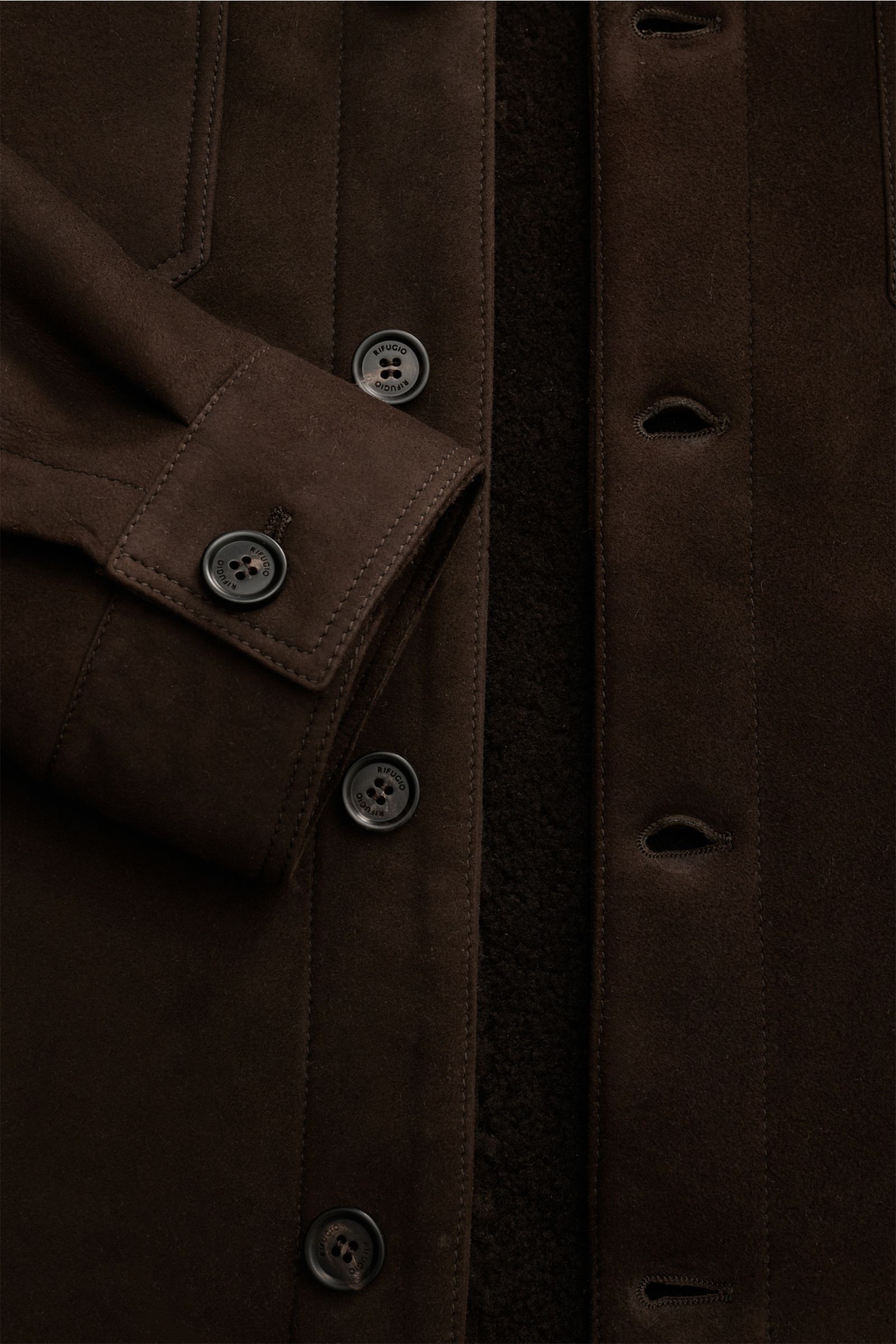 Nahaufnahme der Rifugio Lammfelljacke dunkelbraun von vorne, zeigt geschmeidiges Veloursleder, Innenseite aus Lammfell, Slim Fit, sechs Knöpfe, Umlegekragen, Brusttaschen mit Patte, Ärmel mit Manschette und Knopf, weicher Griff.