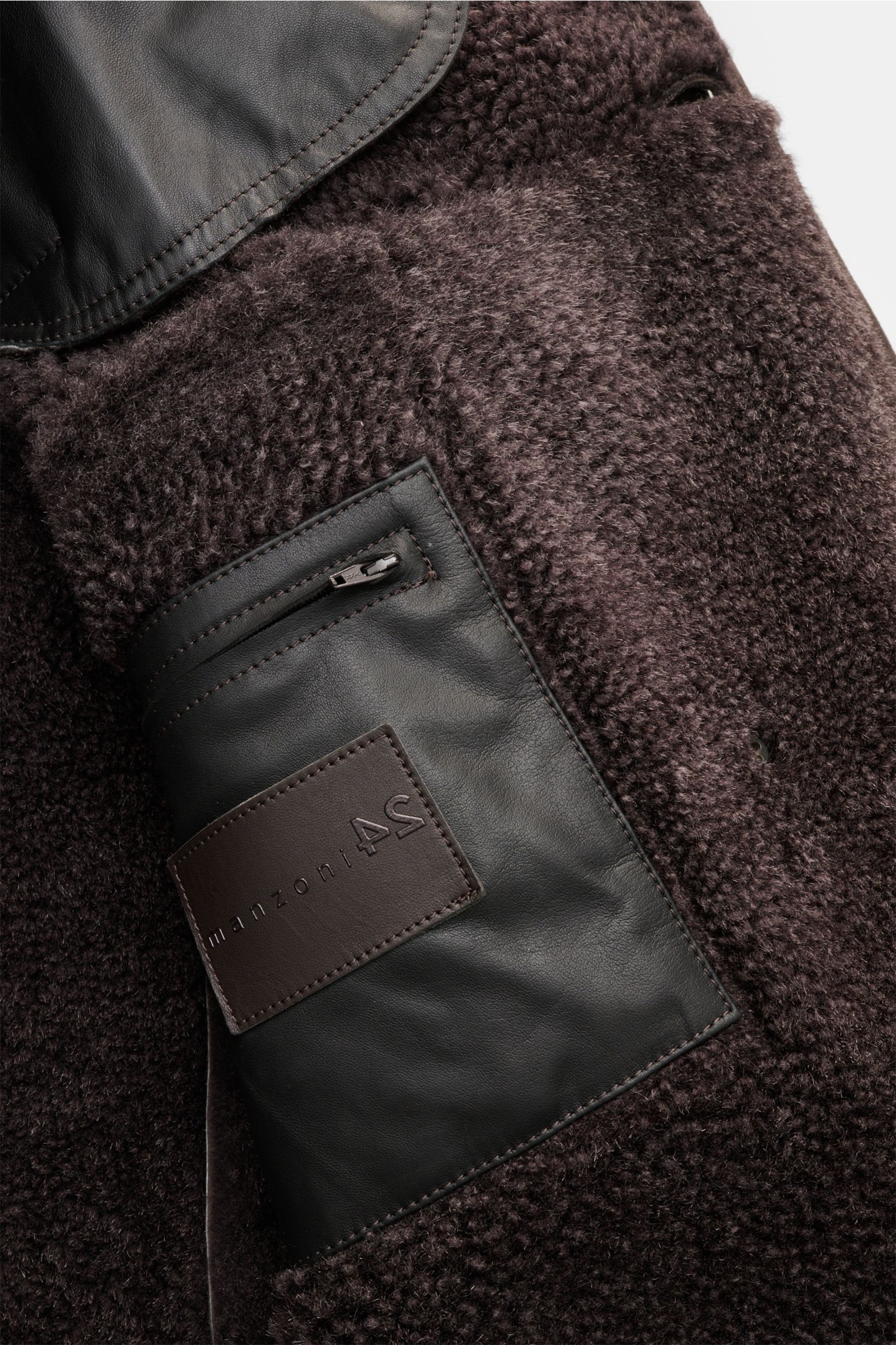 Nahaufnahme des Manzoni 24 Lammfellmantels dunkelbraun aus weichem Lammveloursleder mit Reverskragen, Innentasche und Lammfell-Innenseite.