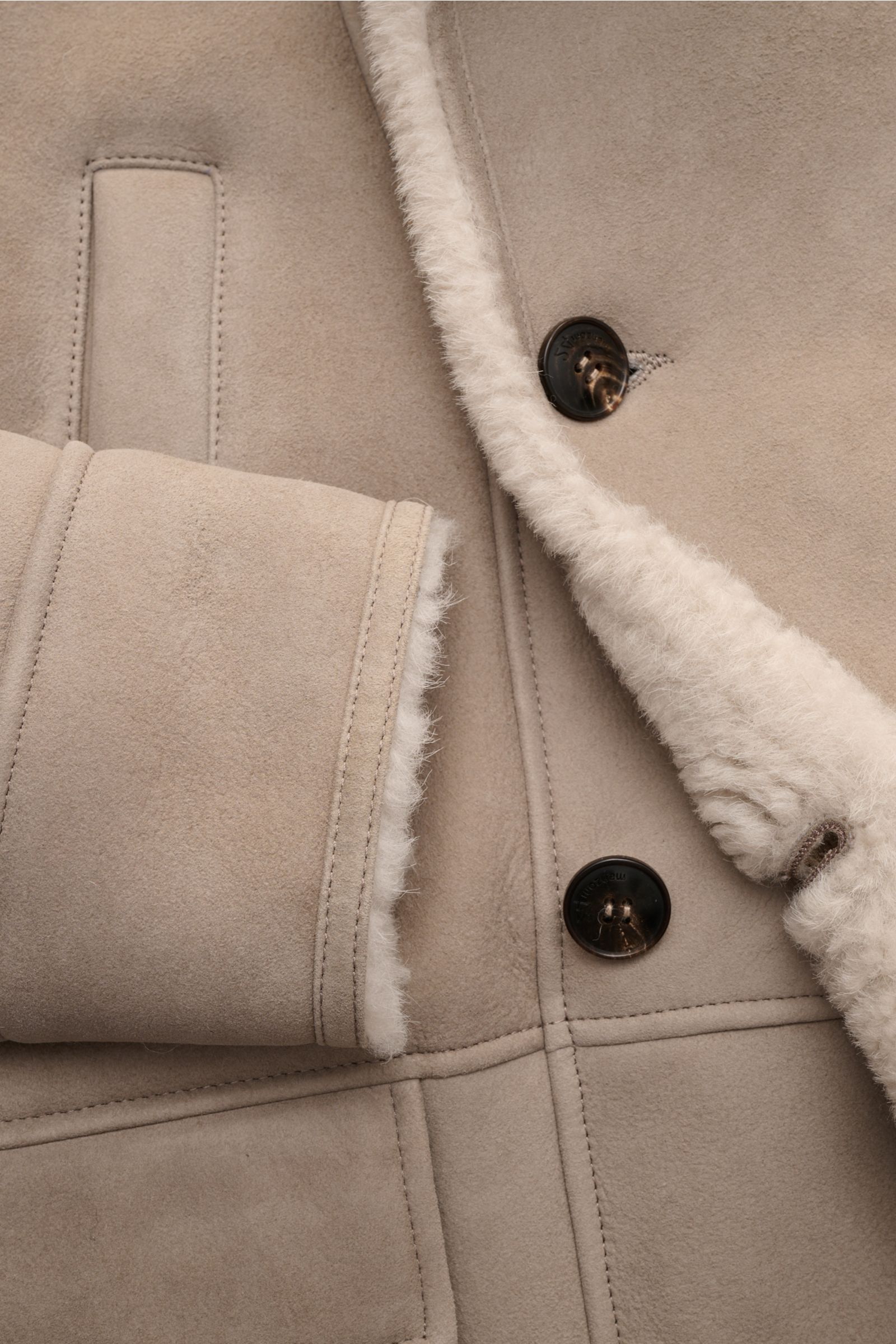Close-up view of the Manzoni 24 Lammfelljacke hellgrau showing soft light grey lamb velour leather, warm lamb fleece lining, button details, and stitching. Der Luxus von wärmendem Lammfell materialisiert sich in dieser Jacke von MANZONI 24 aus weichem 