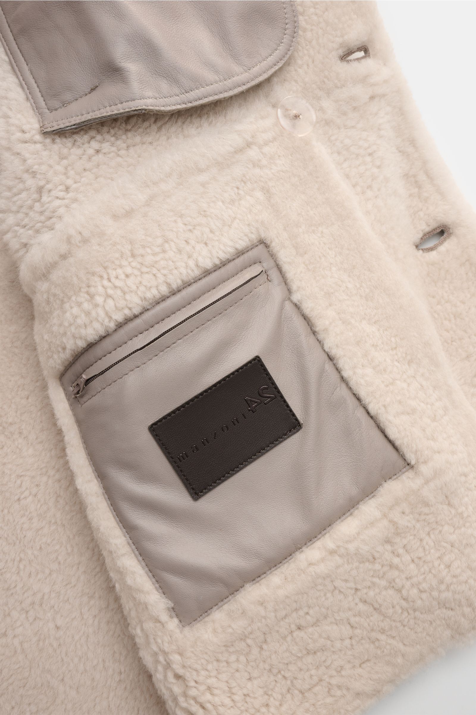 Close-up interior view of the Manzoni 24 Lammfelljacke hellgrau showing soft lambshear lining, leather inner pocket with zipper, and buttonhole details, highlighting luxury and craftsmanship.

Description: Der Luxus von wärmendem Lammfell materialisier