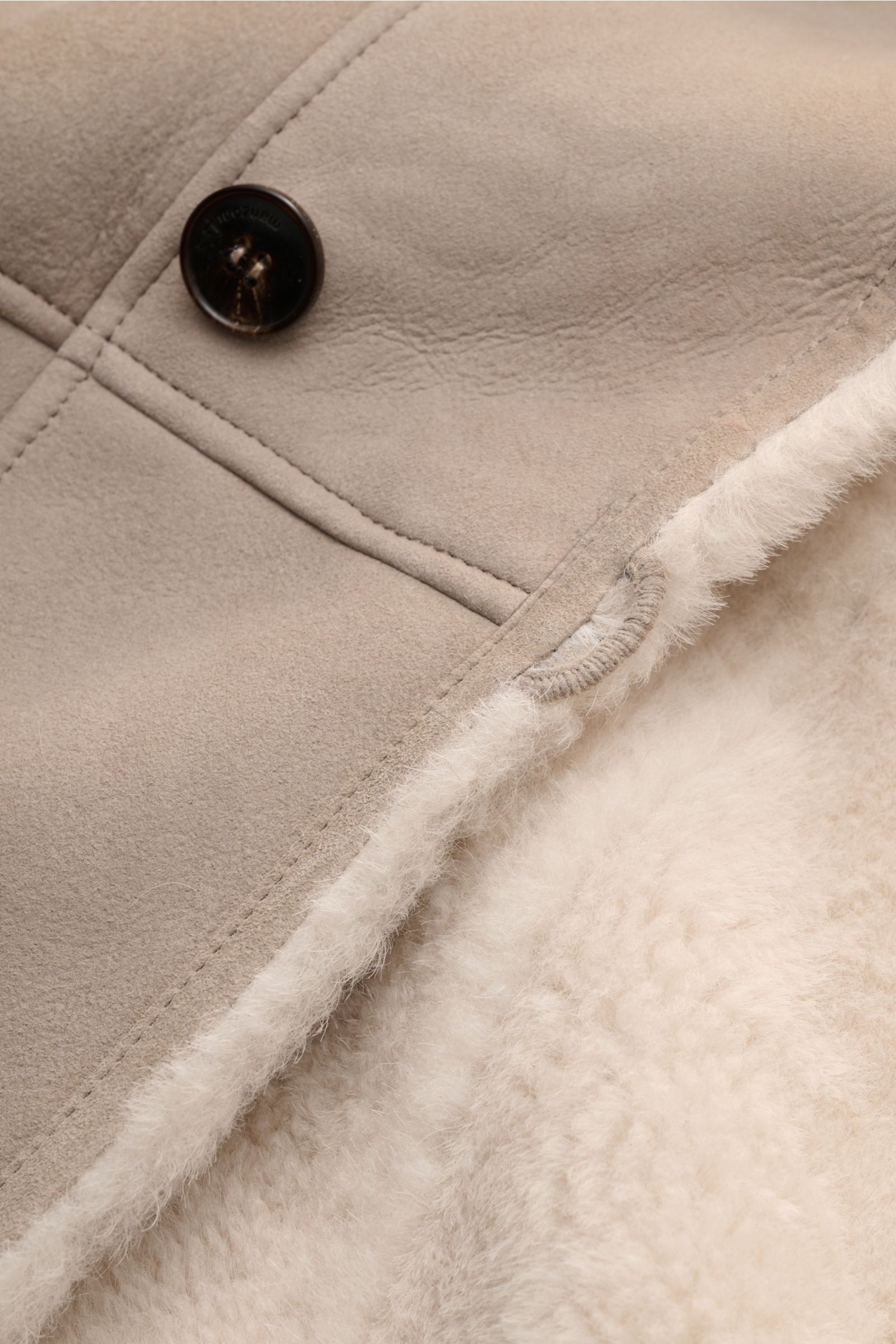 Close-up from above of the Manzoni 24 Lammfelljacke hellgrau showing soft grey lamb suede with a dark button and warm cream lambskin lining; Der Luxus von wärmendem Lammfell materialisiert sich in dieser Jacke von MANZONI 24 aus weichem Veloursleder mit v