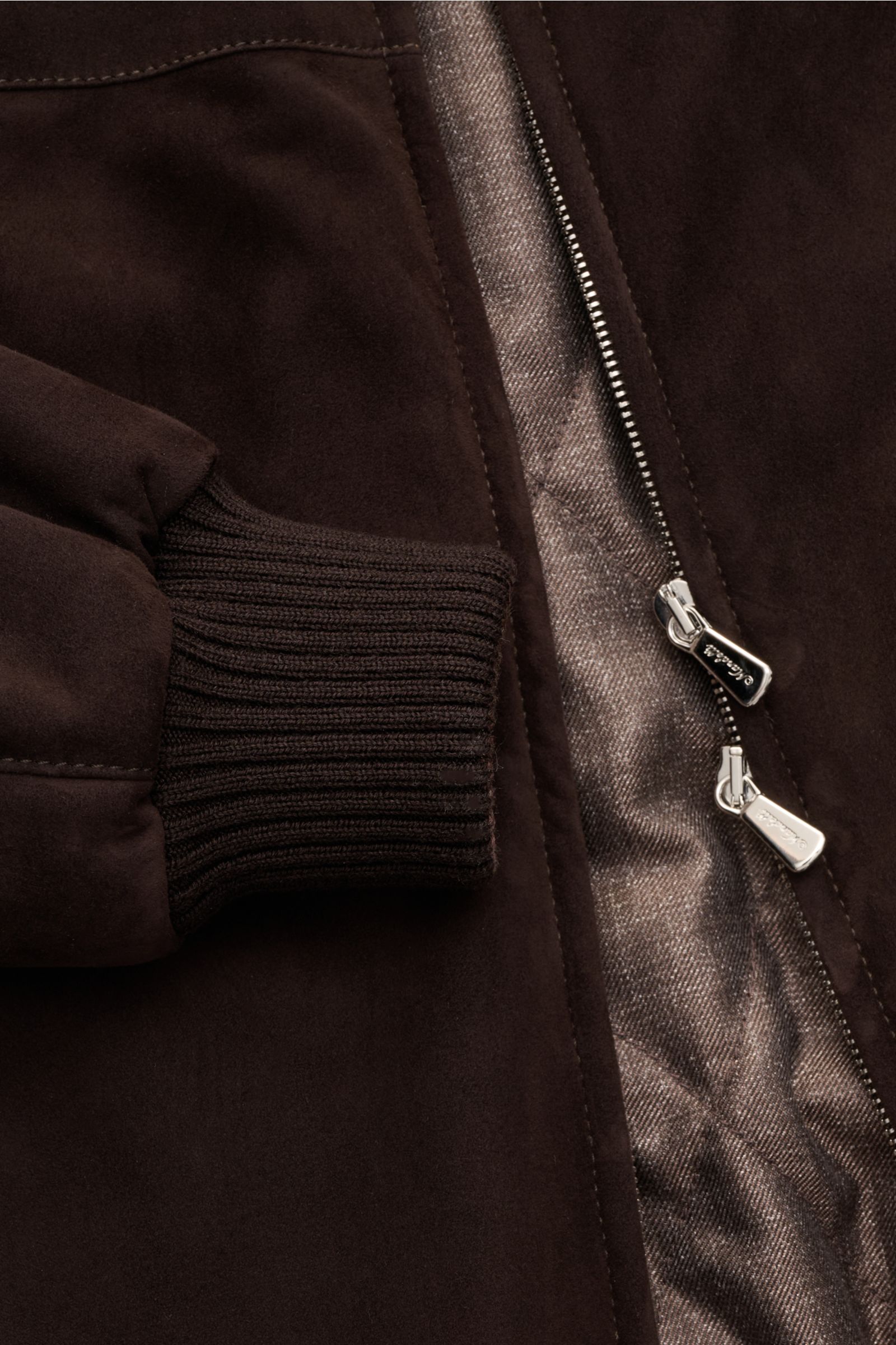 Close-up shot of the Mandelli Veloursleder-Blouson dunkelbraun showing its soft dark brown goat suede, ribbed elastic sleeve cuff, and two-way silver zipper with quilted lining. Luxuriöser Komfort für die Übergangszeit: Der Veloursleder-Blouson von MANDEL