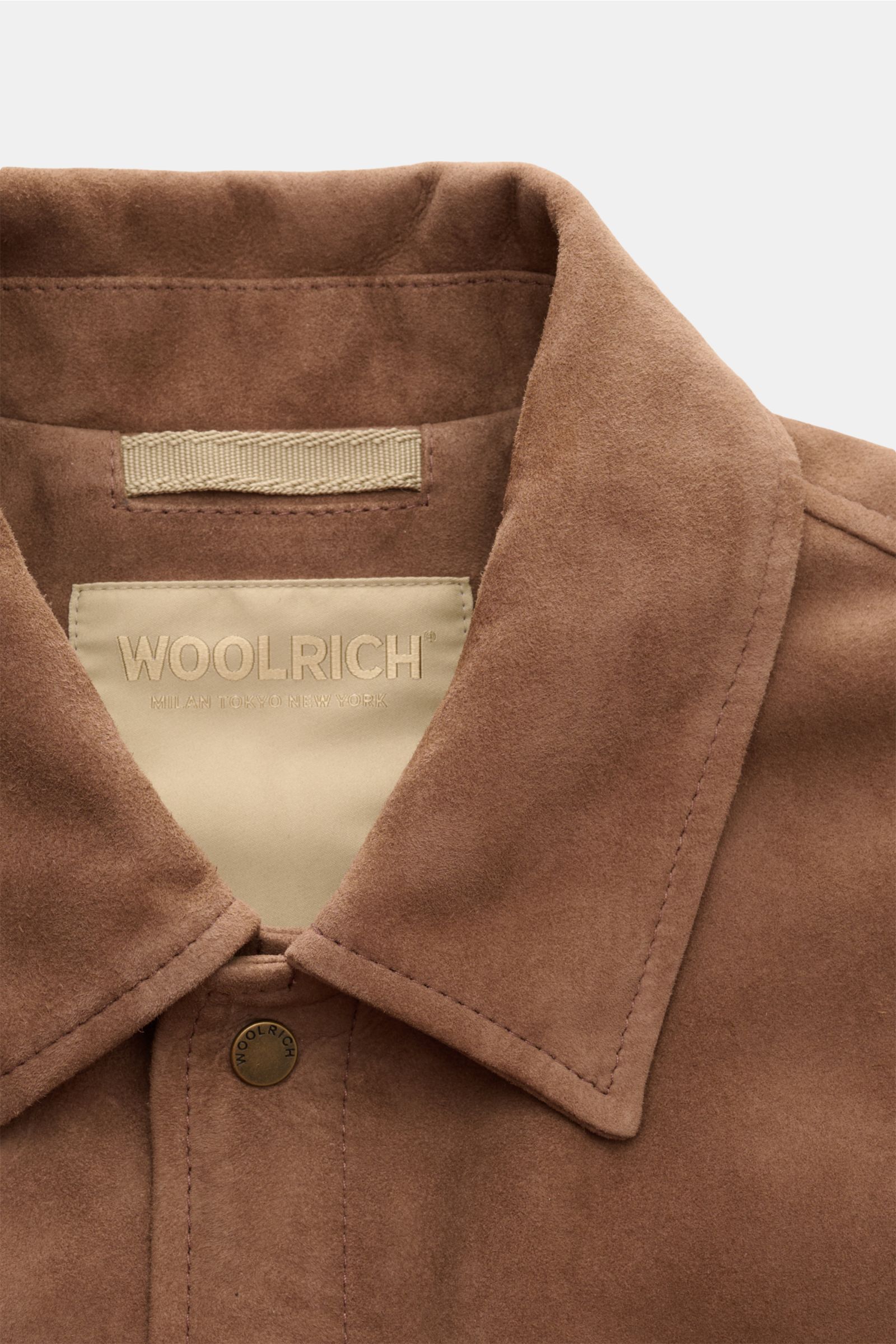 Nahaufnahme im Detail der braunen Woolrich Veloursleder-Daunenjacke mit Umlegekragen, Druckknopfleiste und weichem Ziegenvelours.