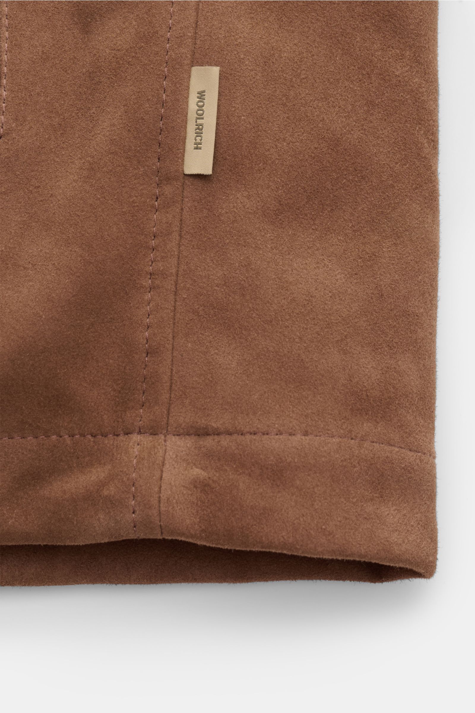 Nahaufnahme der braunen Woolrich Veloursleder-Daunenjacke aus softem Ziegenveloursleder mit Nahtdetails und Woolrich-Label, Frontansicht.