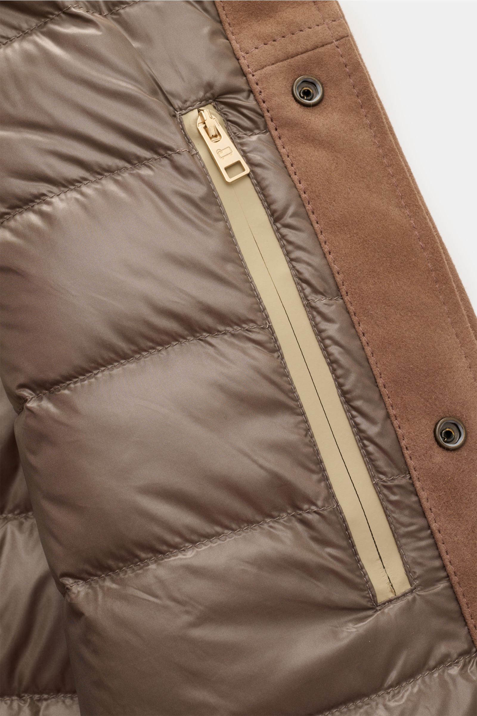 Nahaufnahme der Innenseite der Woolrich Veloursleder-Daunenjacke braun, zeigt gesteppte Daunenfüllung, Innentasche mit Reißverschluss und Druckknopfleiste aus softem Ziegenveloursleder.