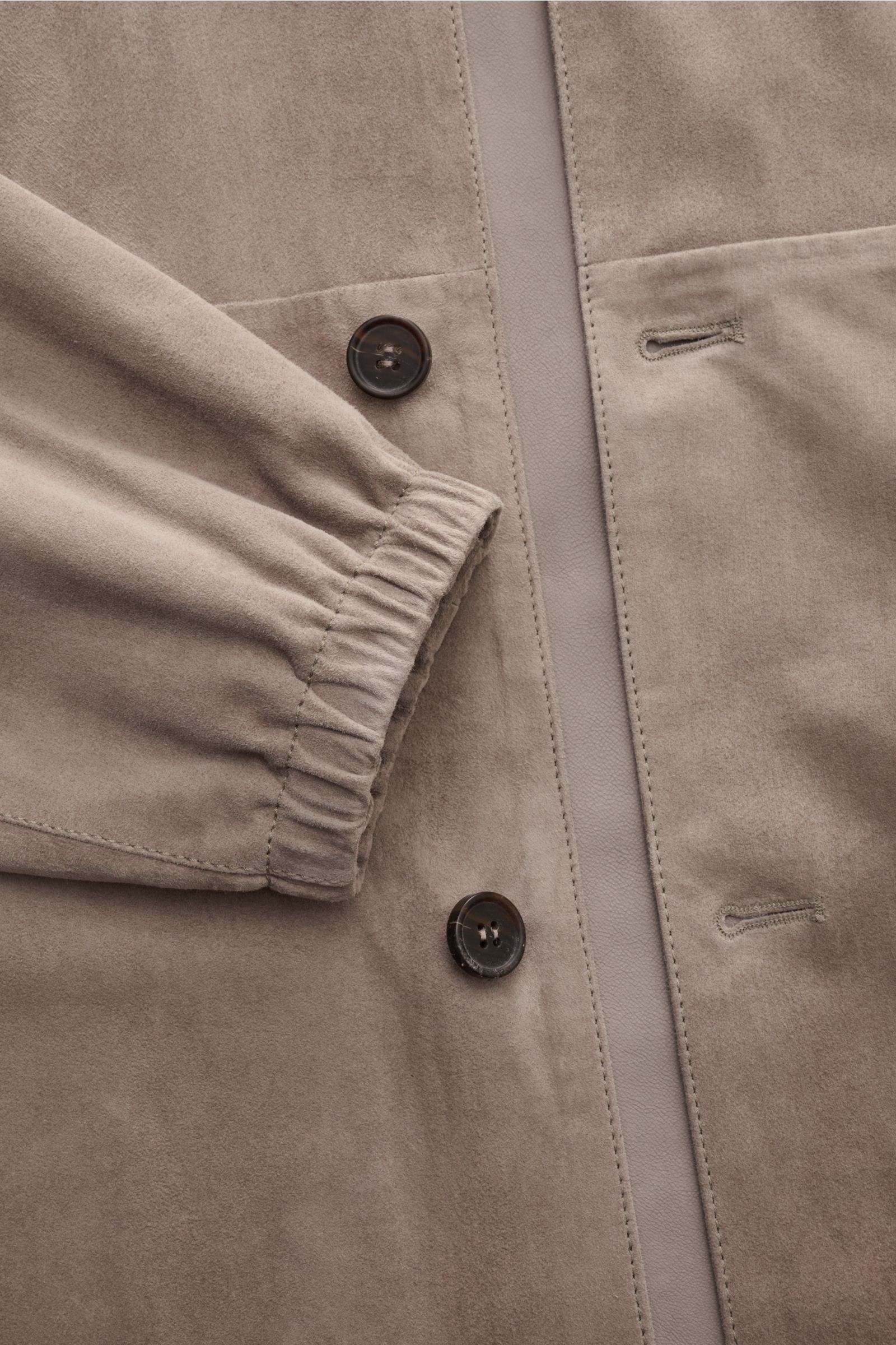 Close-up front view of Emporio Armani Velourslederjacke taupe showing soft taupe goat suede, five-button placket, elastic sleeve cuff, and detailed stitching. Urbaner Allrounder: Die Velourslederjacke von EMPORIO ARMANI kombiniert legeren Stil mit praktis