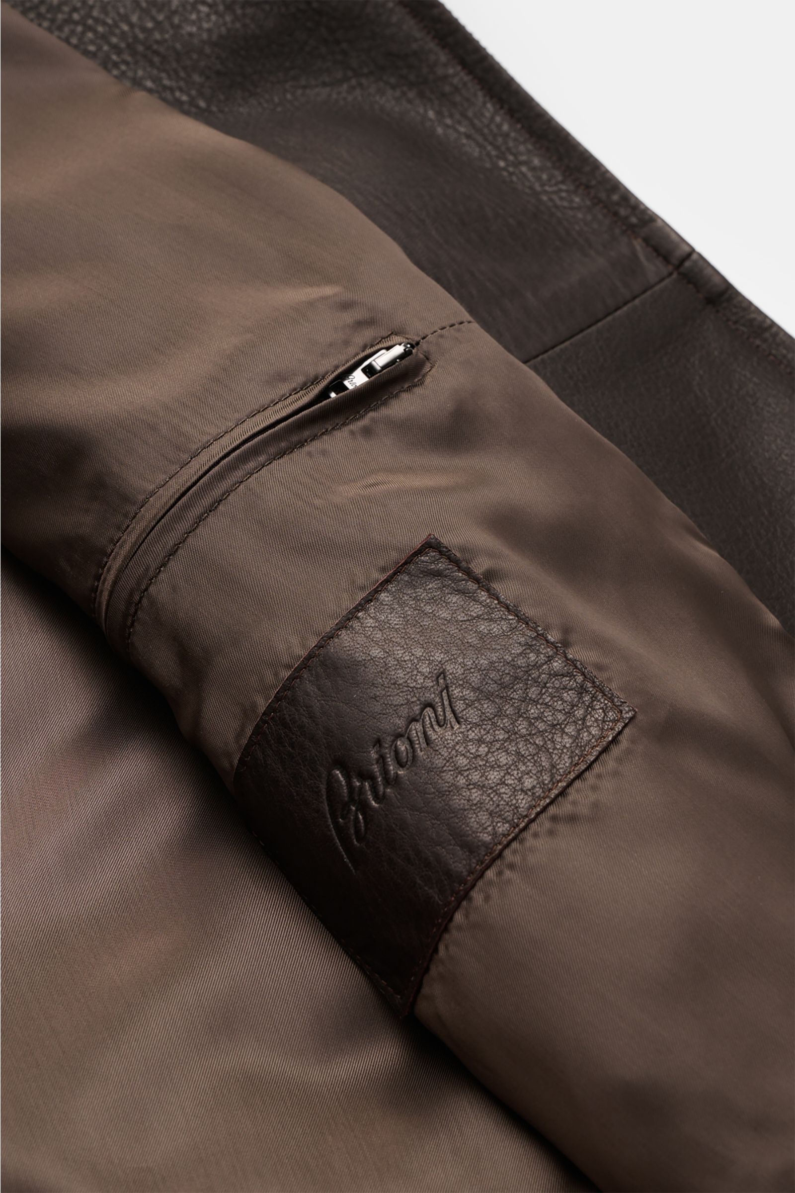 Close-up inside view of the Brioni Leather blouson 'Plad' dark brown showing smooth lining, zippered inside pocket, and branded leather patch; a statement in fine craftsmanship with elegant lambskin leather, slim fit, two-way zip, zip front pockets, elast