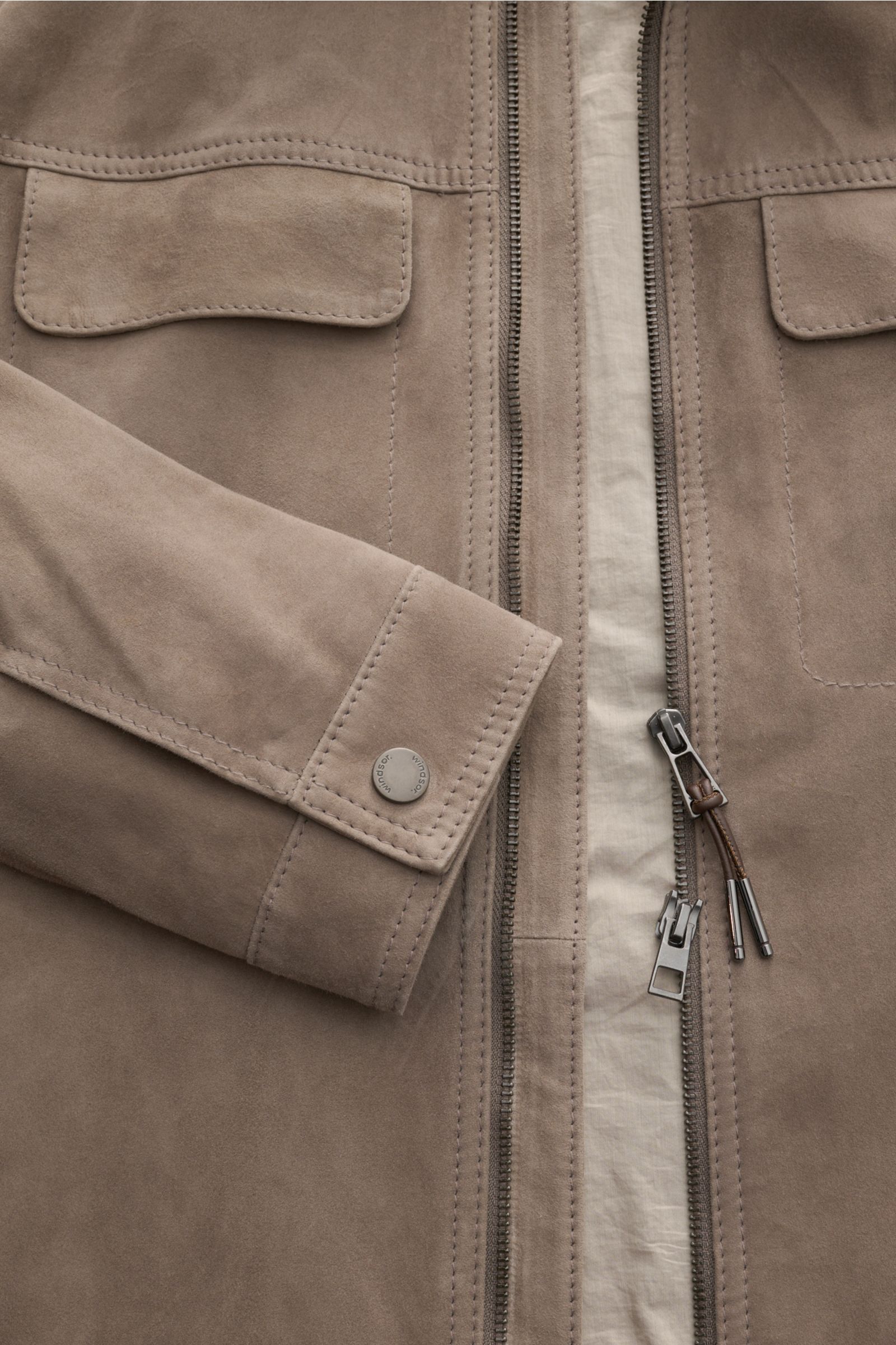 Nahaufnahme der Windsor Lederjacke 'Pesaro' taupe aus softem Veloursleder, mit Reißverschluss, Umlegekragen, Brusttaschen mit Patte und Manschette mit Druckknopf, fotografiert von vorne.