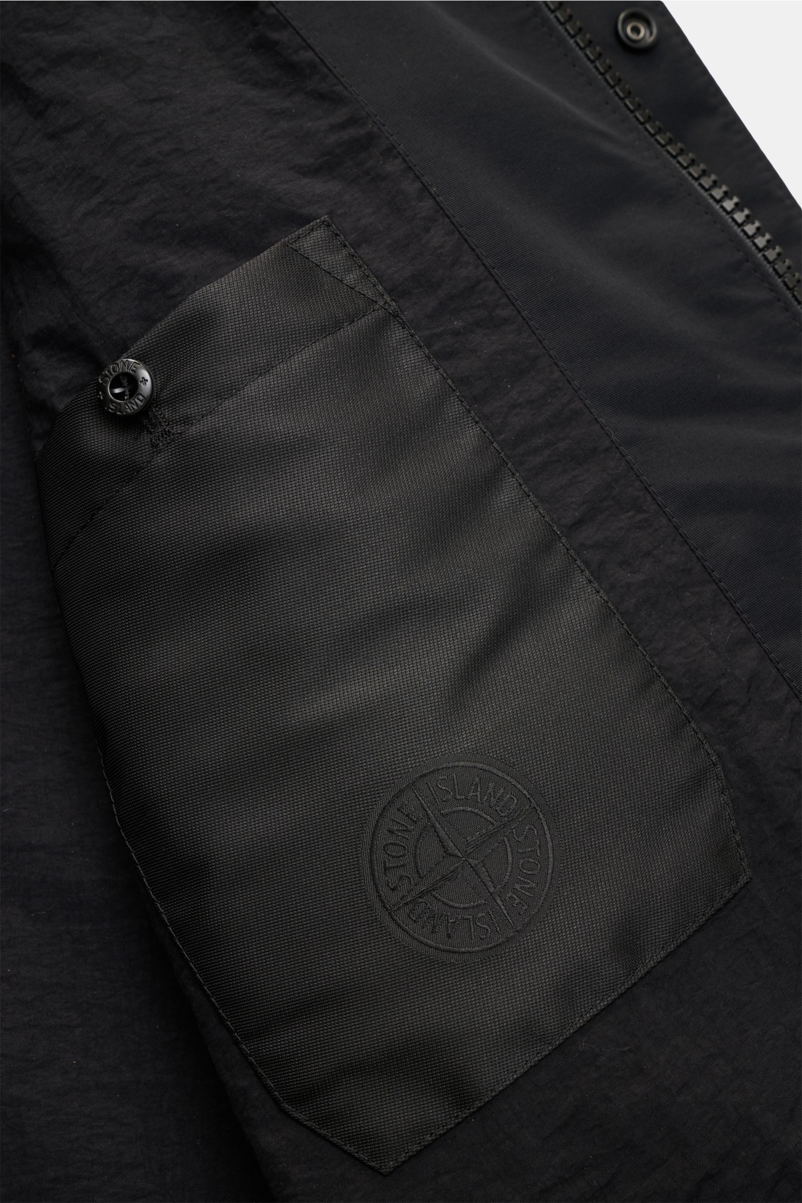 Stone Island Velourslederjacke 'Ghost Piece' schwarz, Detailfoto der aufgesetzten Fronttasche mit Logo-Button, feine Materialstruktur.